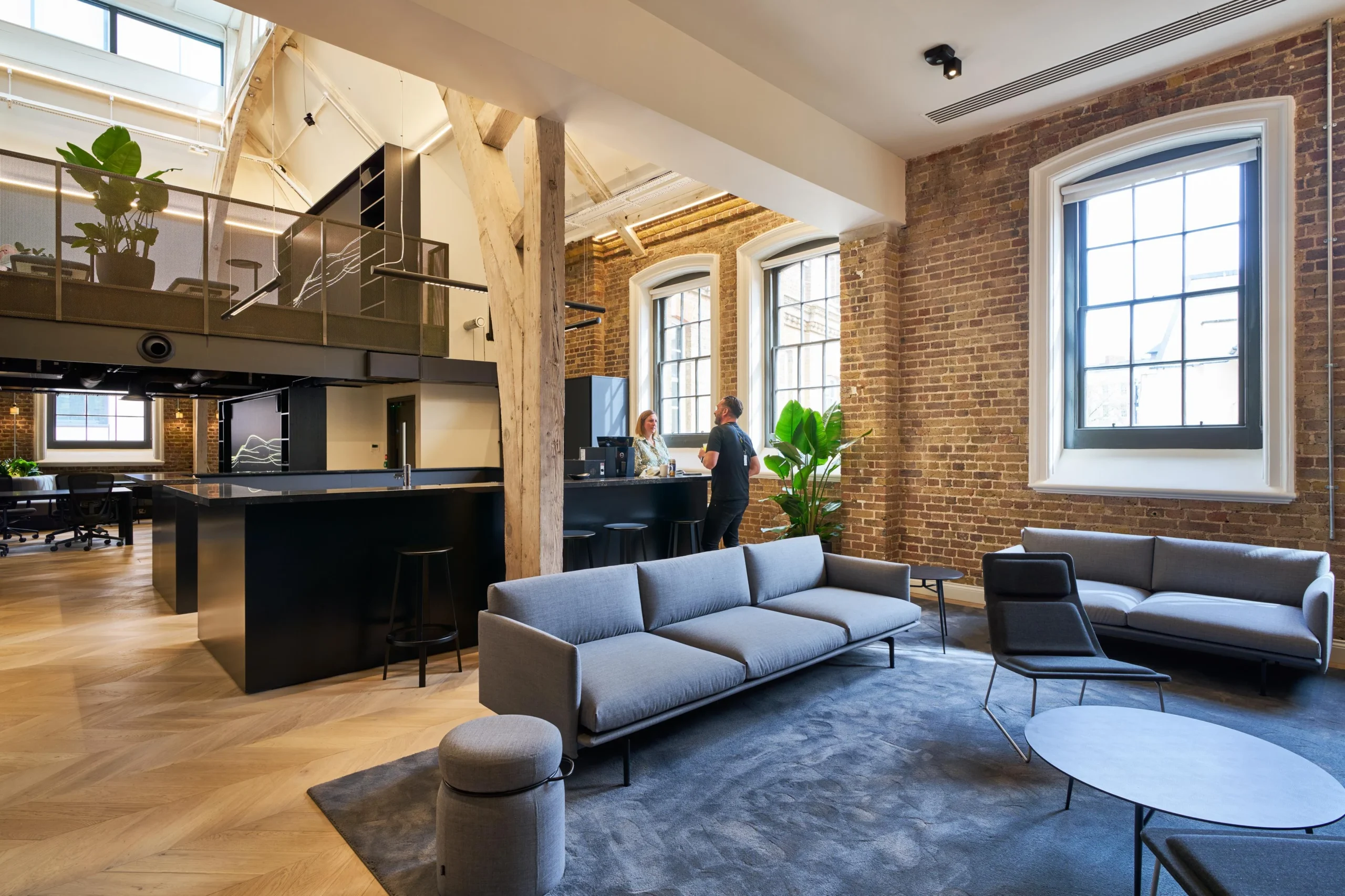 Breakout furniture installed for Lotus, with modern sofas and low tables styled within a brick-walled breakout space beside an open kitchen.