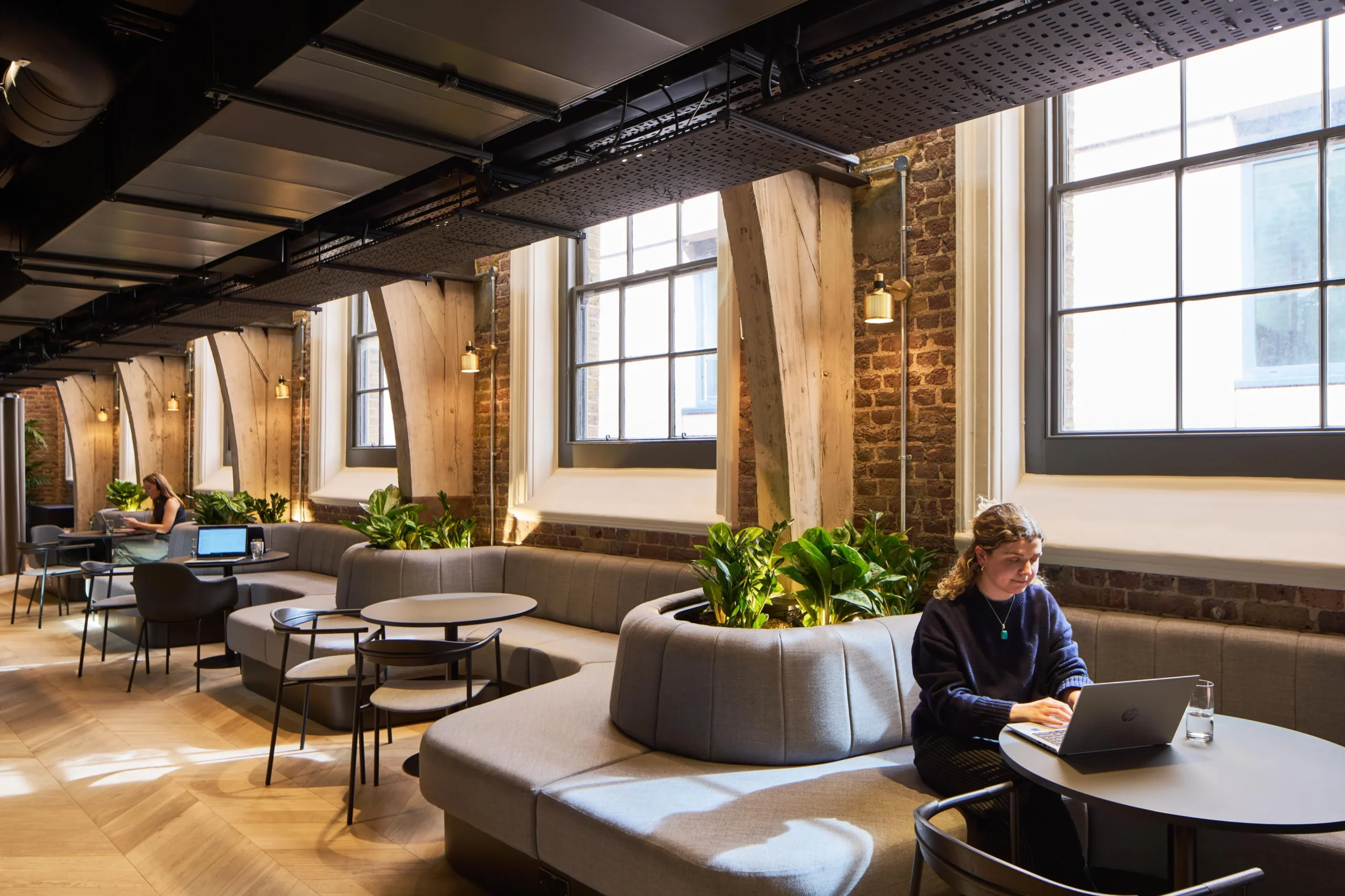 Curved banquette seating and café tables supplied for Lotus, styled along exposed brick and timber beams with integrated planters for a biophilic touch.