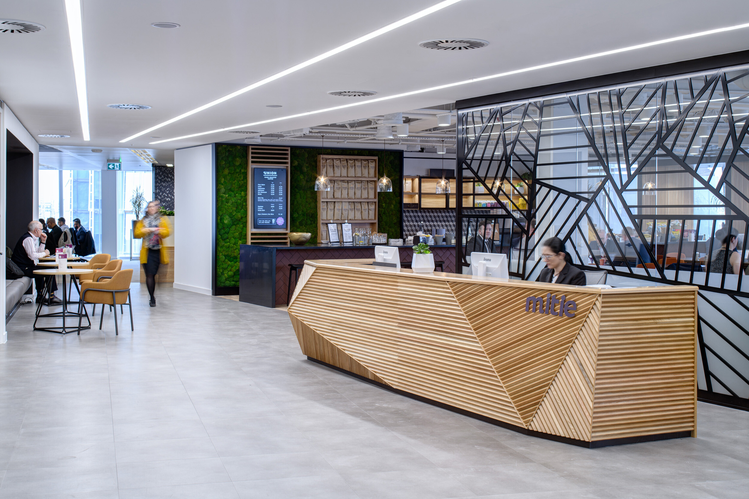 Reception area at MITIE's Shard office featuring a geometric timber desk, black partitioning, and lounge furniture supplied by Platfform.
