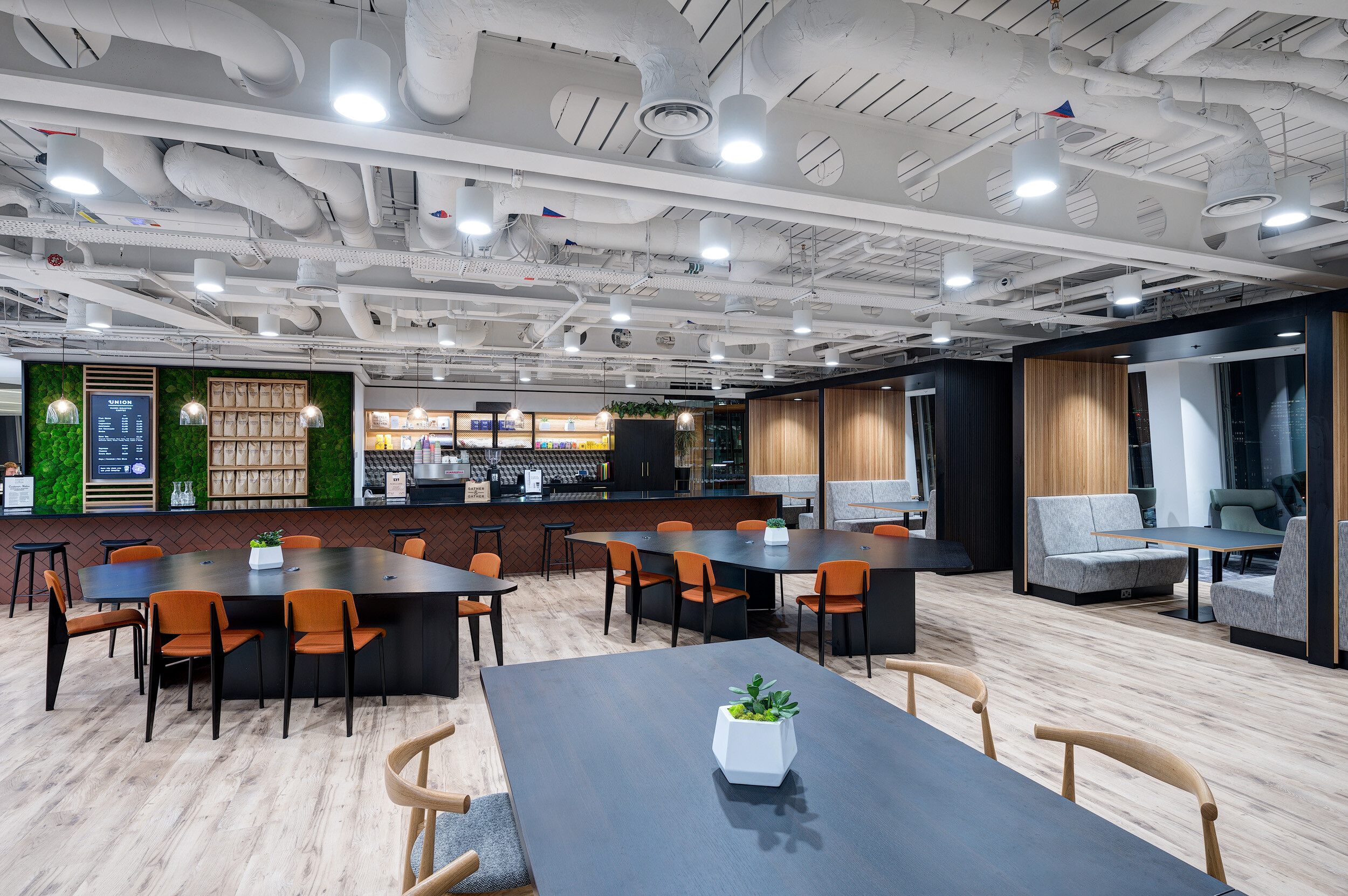 Café-style breakout space at MITIE's Shard office with dark communal tables, orange chairs, and booth seating furnished by Platfform.