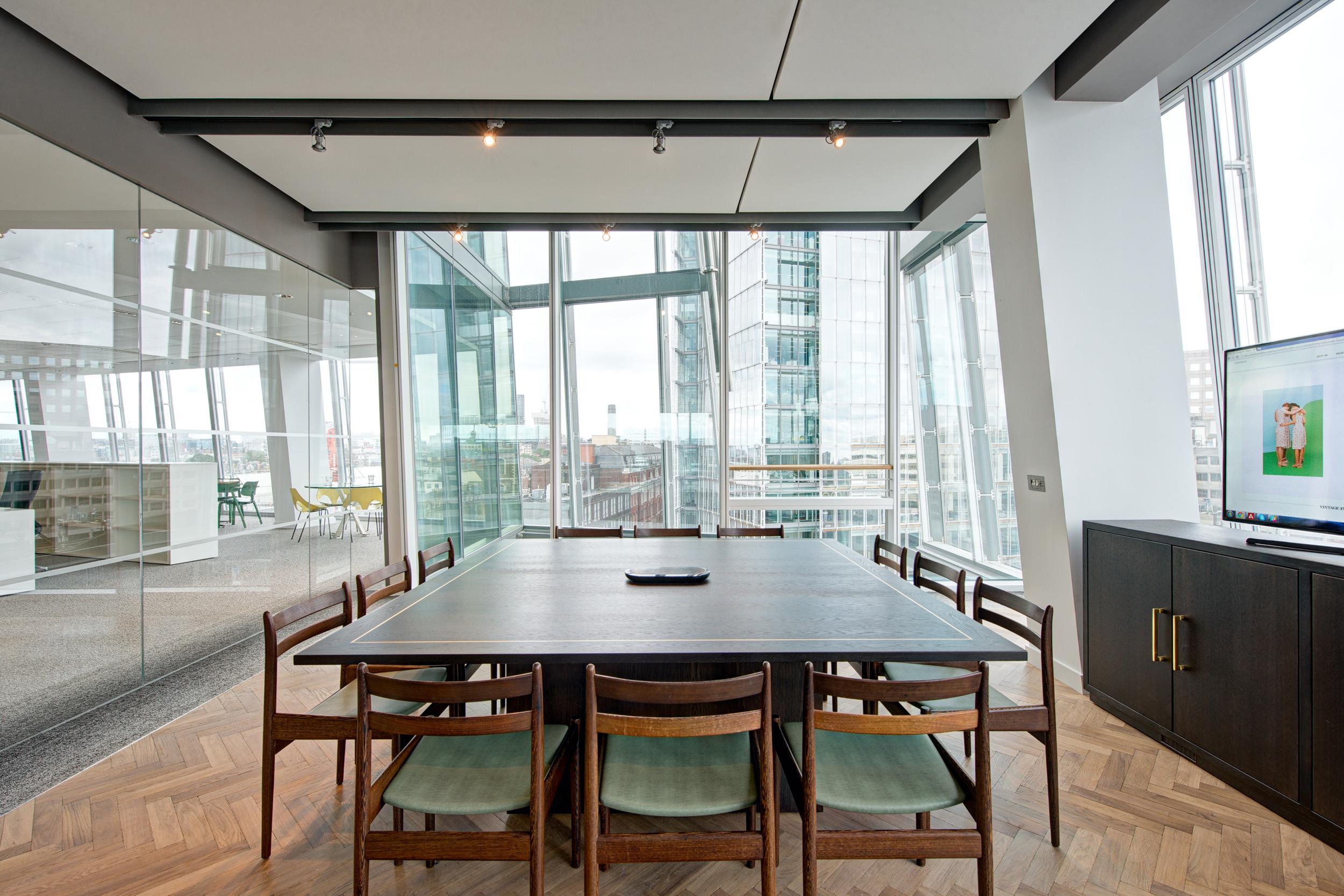 Meeting room furniture for Matches Fashion, featuring a dark timber meeting table and matching chairs with green seat pads in a glass-walled office with city views.