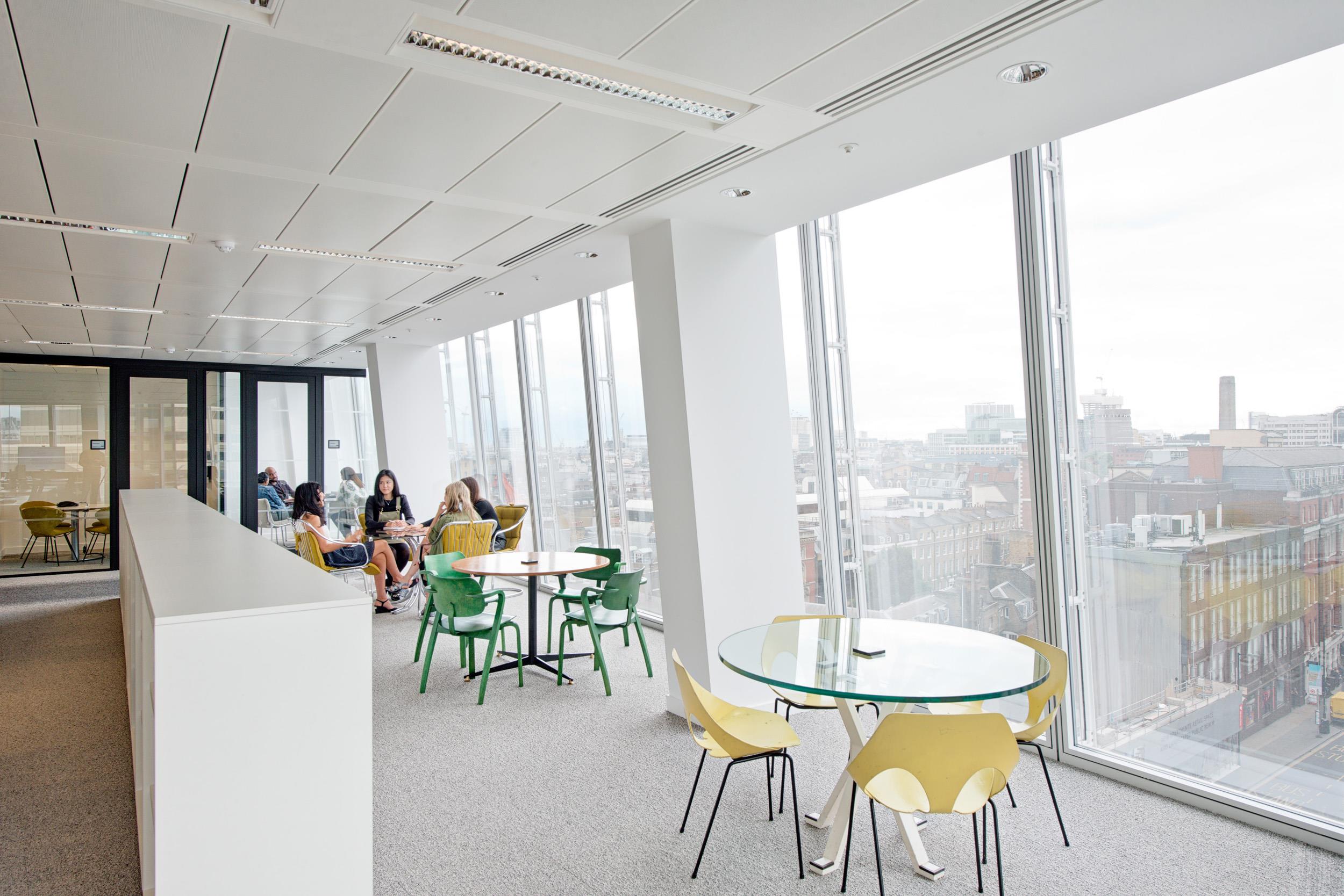 Lounge and breakout area at Matches Fashion, furnished with colourful café-style chairs and glass-topped tables overlooking the London skyline.