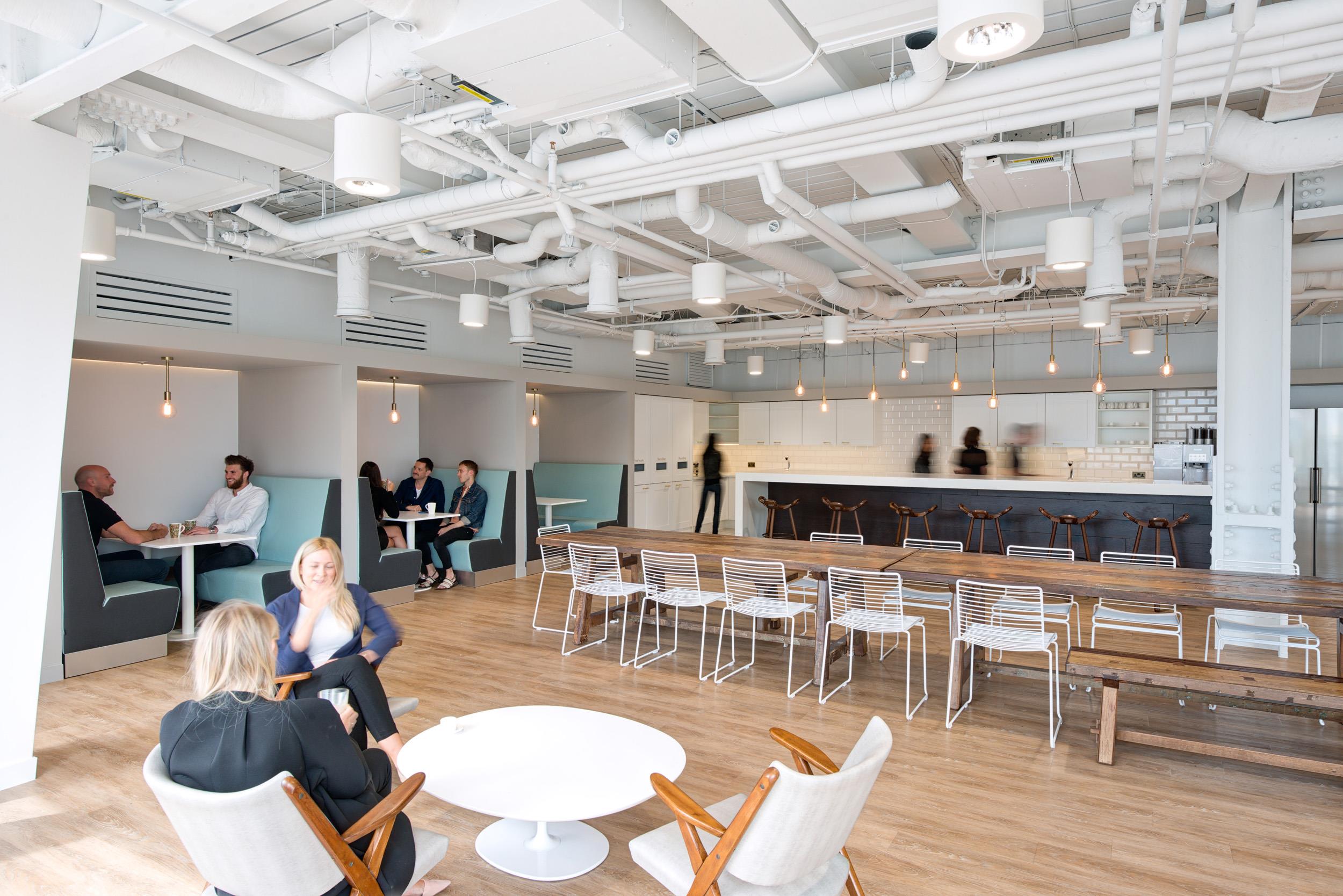 Social hub at Matches Fashion, with built-in dining booths, lounge chairs, and communal tables set against an open kitchen and industrial-style ceiling.