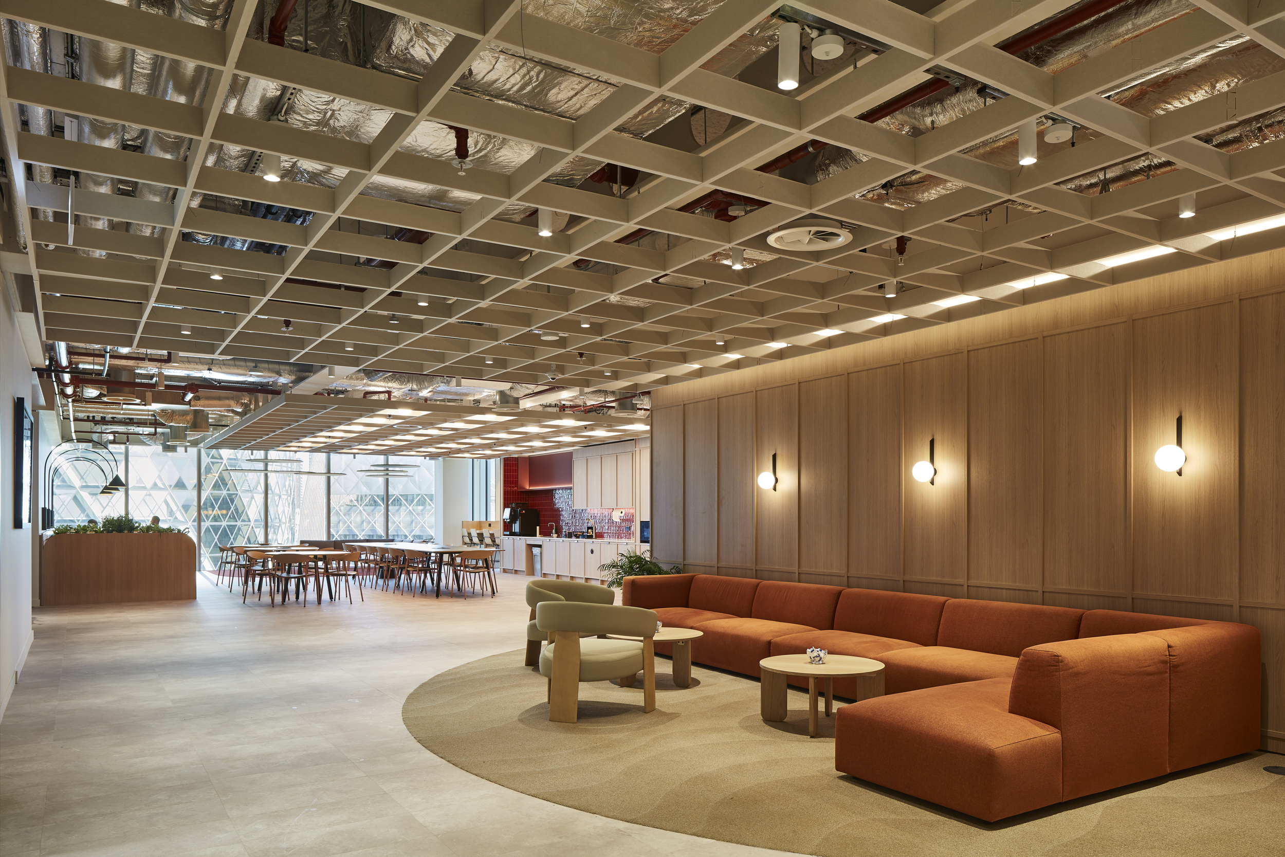 Breakout space at McGill & Partners with Platfform-supplied rust-coloured modular sofa, circular tables, and light timber dining furniture.