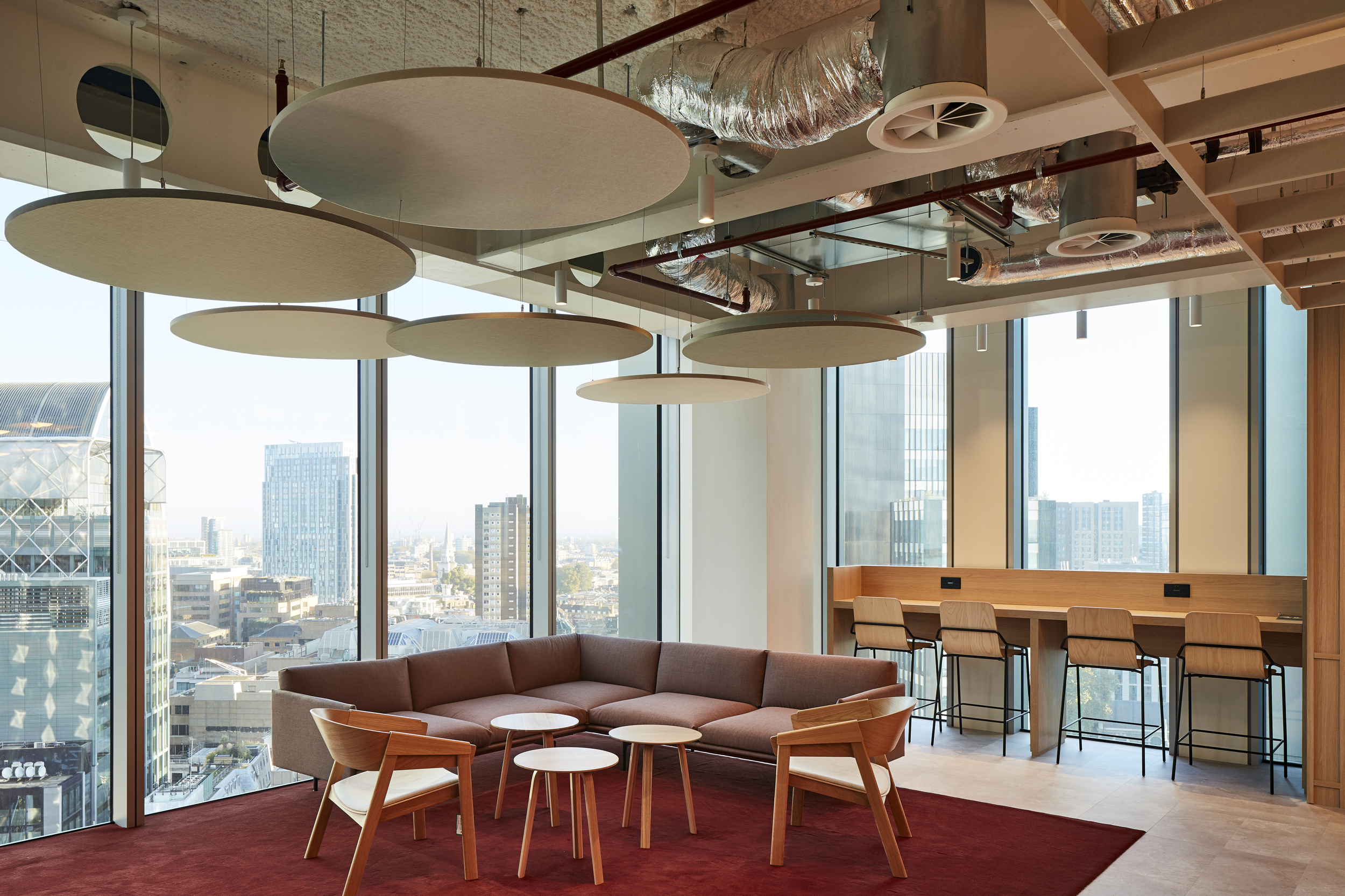 McGill & Partners lounge space furnished by Platfform, with a corner sofa, wooden lounge chairs, and high stools along a built-in desk overlooking the city.