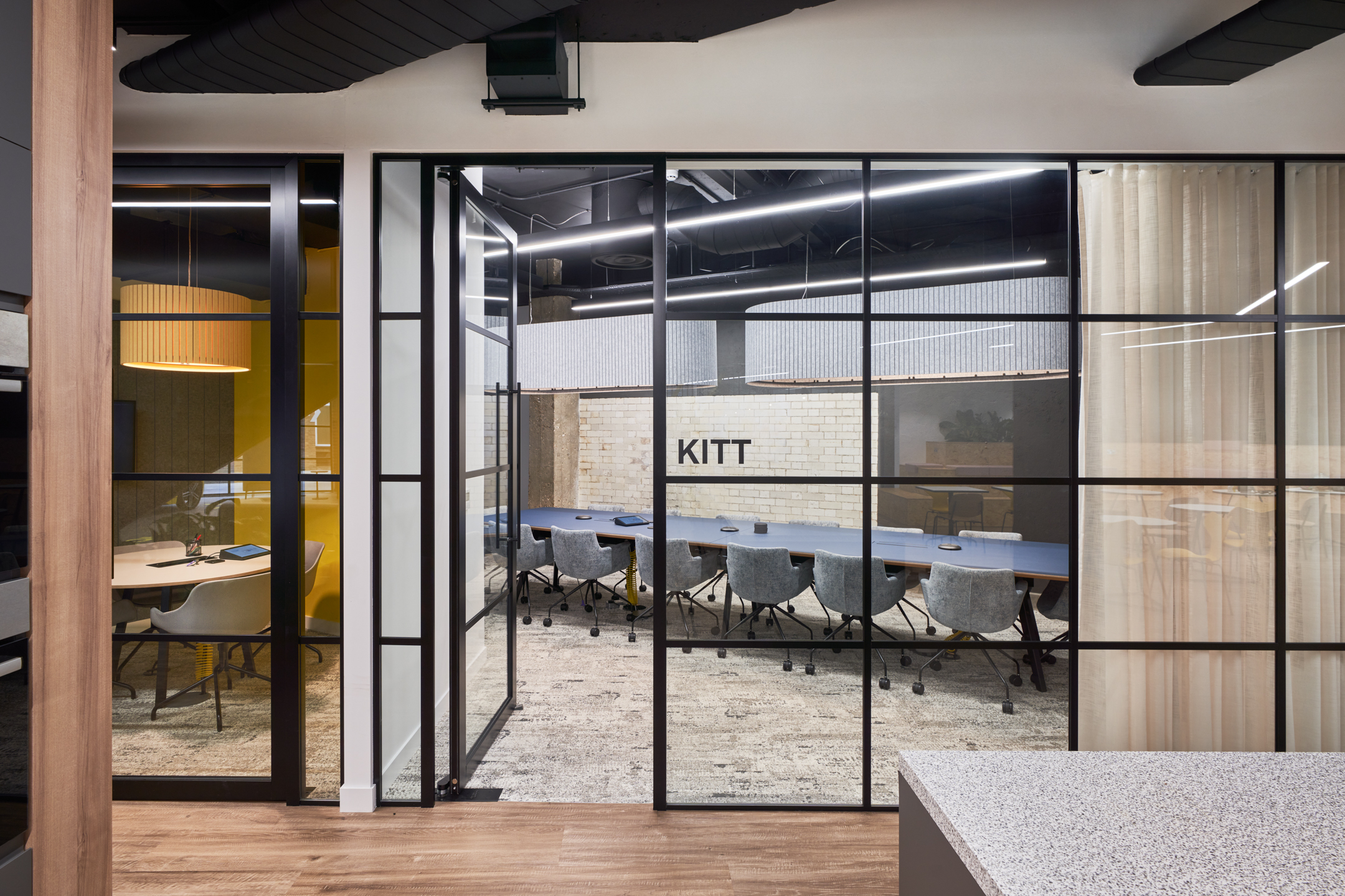 Glazing-fronted meeting rooms at Motorway’s office, furnished by Platfform with grey upholstered chairs and statement boardroom tables designed for collaborative working.