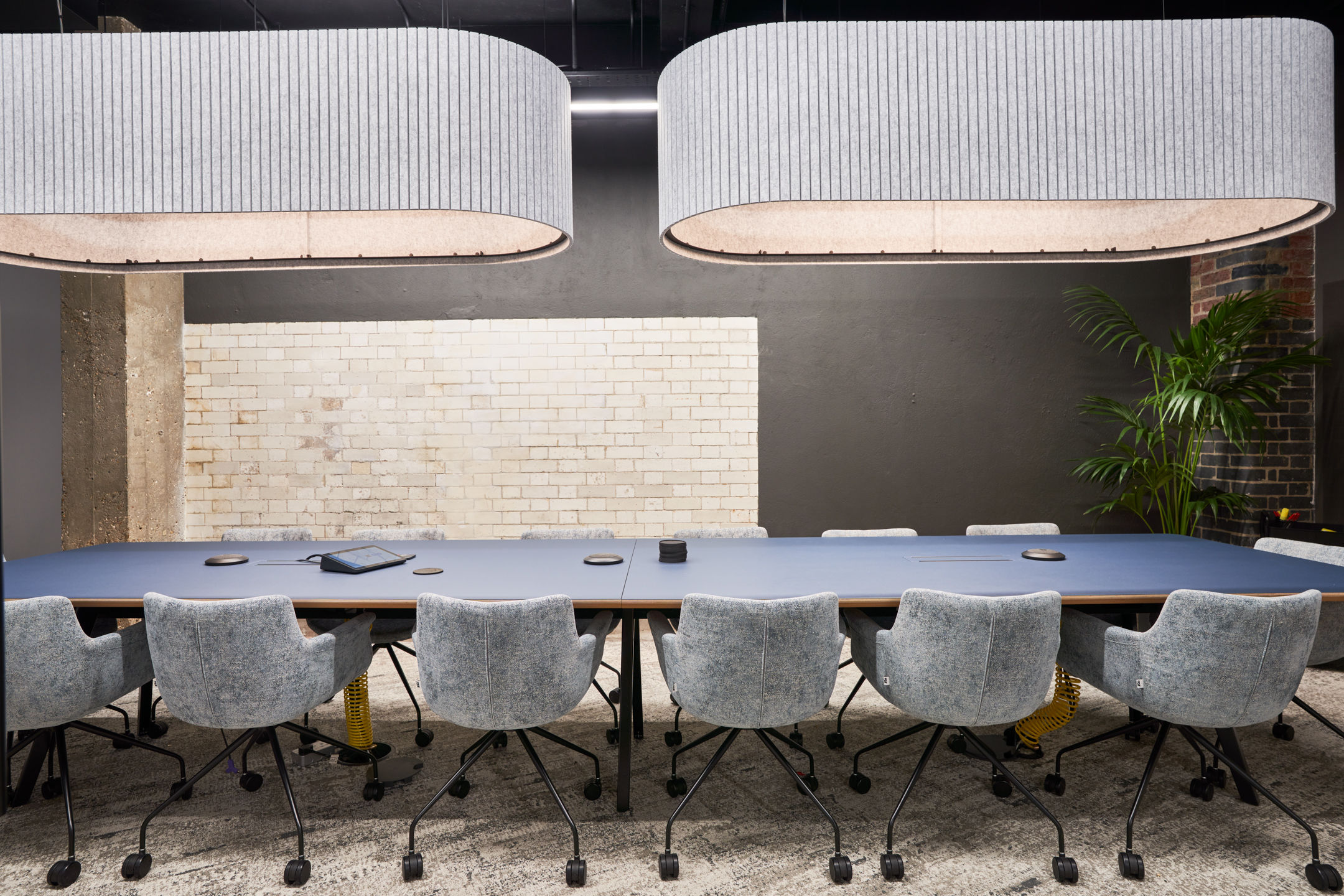 Close-up of the Motorway boardroom furnished by Platfform, showing textured grey meeting chairs, integrated tech, and a matte blue table set beneath oversized acoustic pendants.