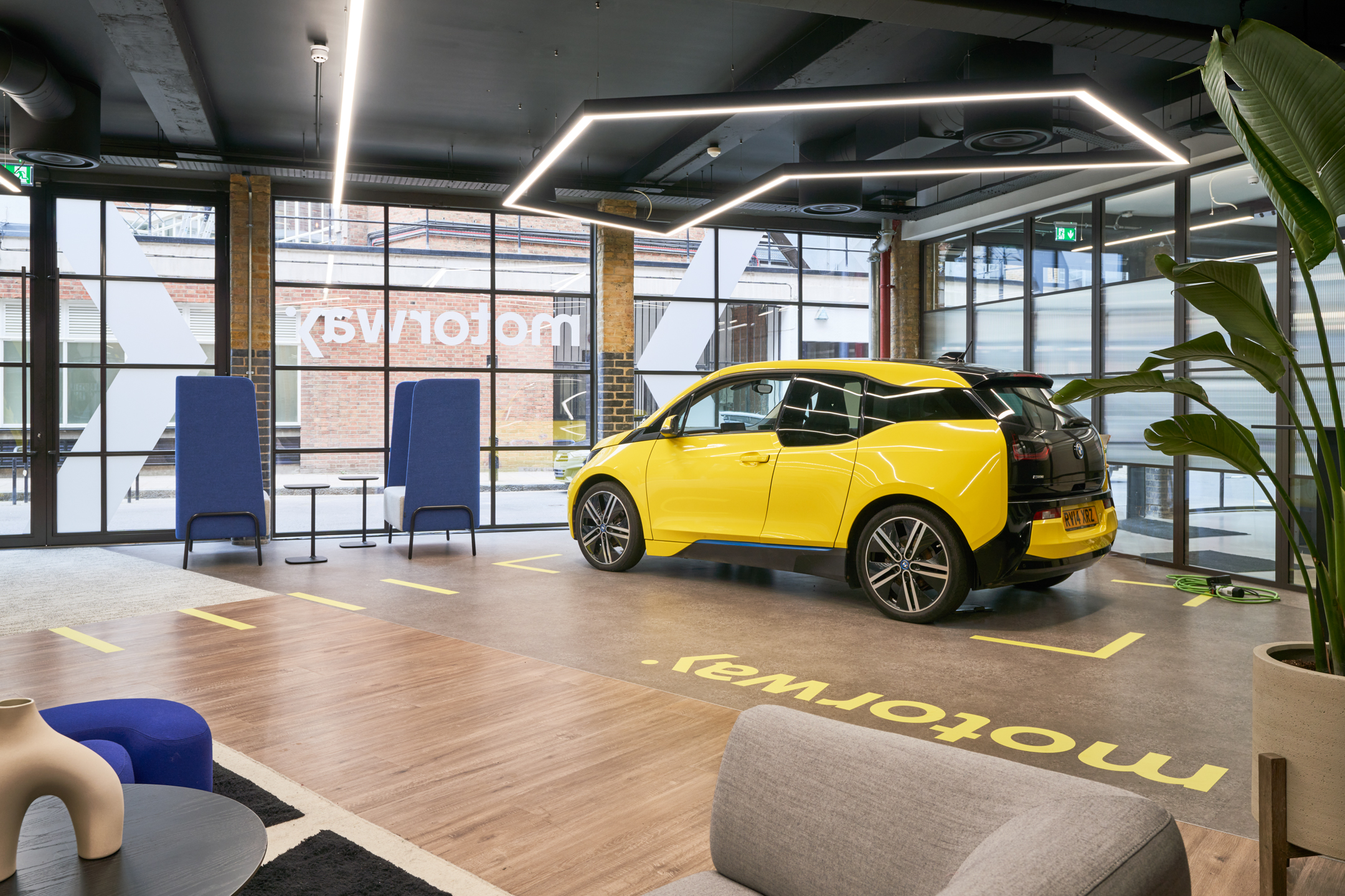 Electric car display inside the Motorway office, styled with modern lounge furniture by Platfform and framed by full-height glazing and branded flooring.
