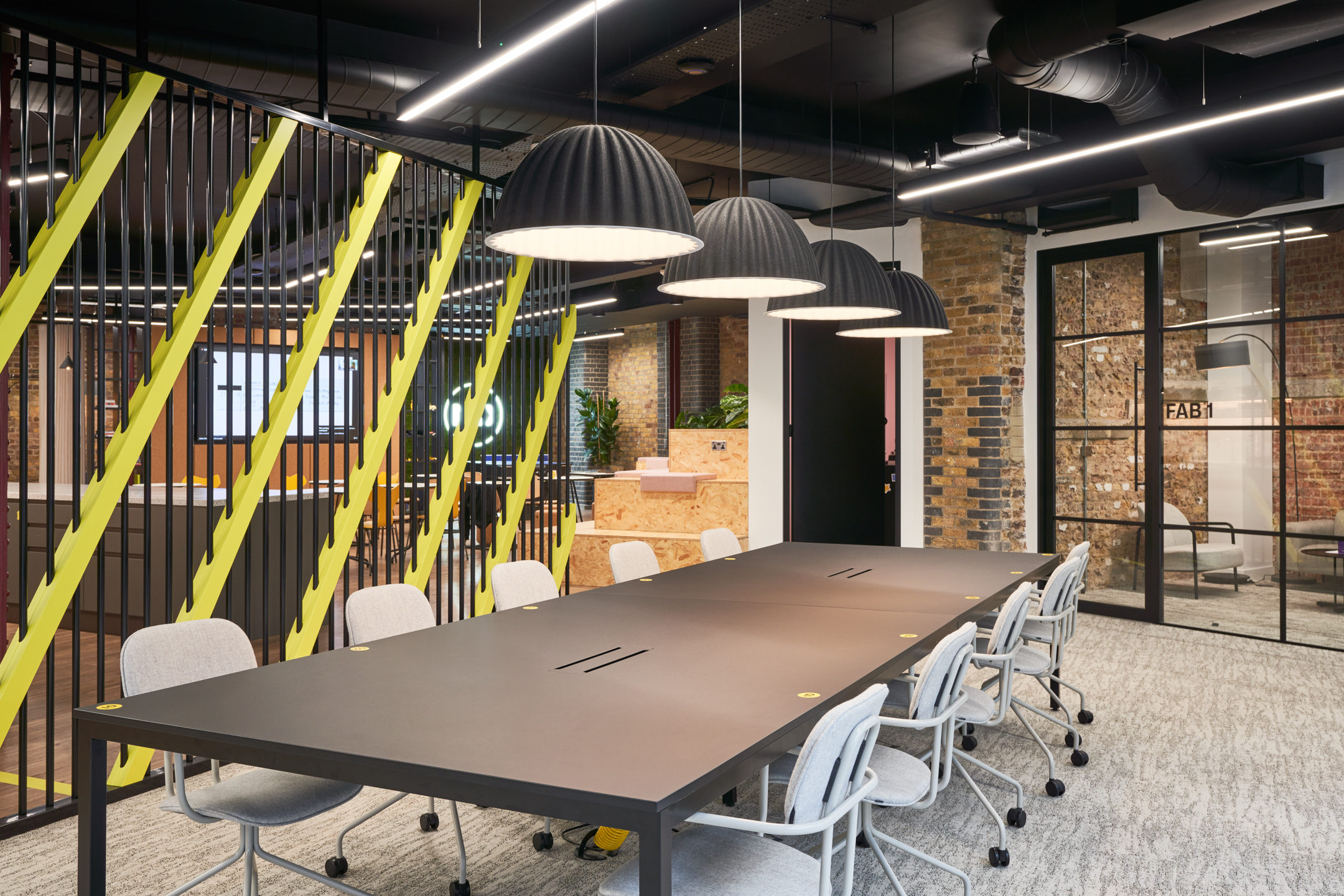 Open-plan workspace at Motorway’s office with shared desking and grey task chairs by Platfform, framed by exposed brickwork and yellow-accented metal partitions.