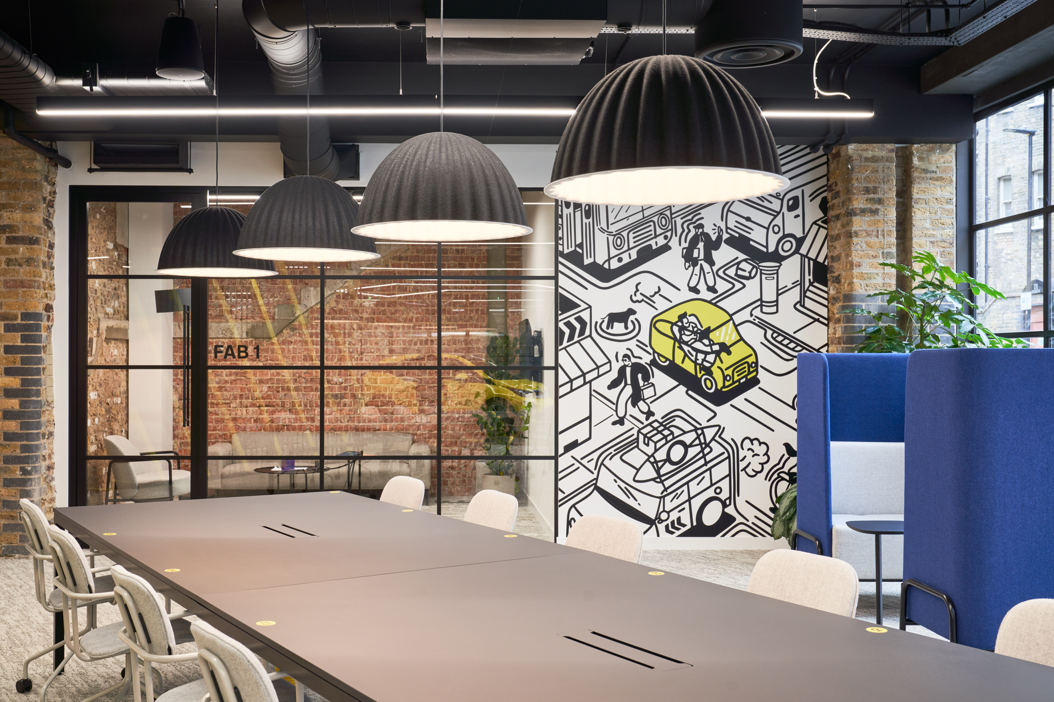 Workspace at Motorway with shared desking by Platfform, a playful transport-themed mural and high-back booths for focused working, set against exposed brick and glazed partitions.