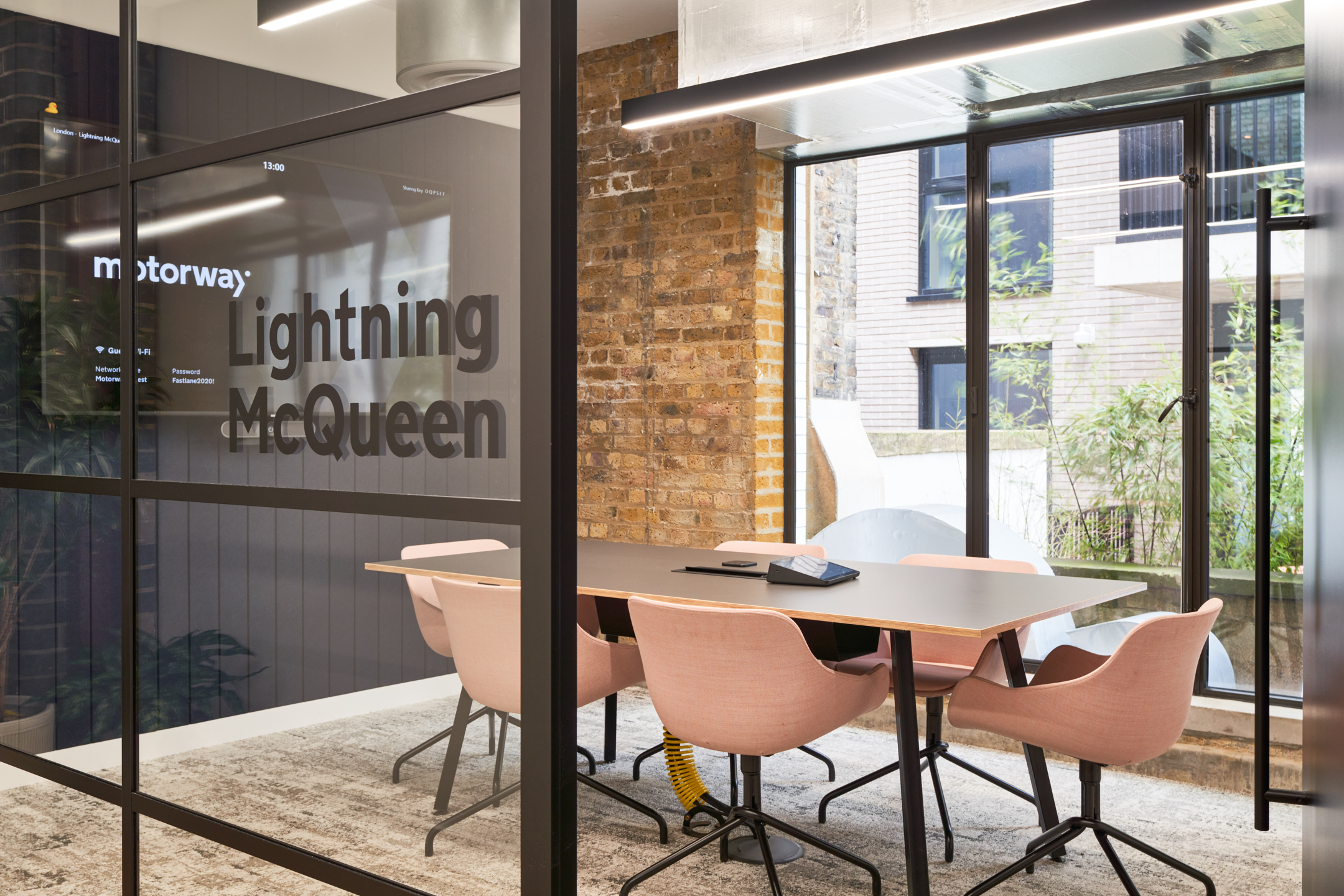 Glass-fronted meeting room at Motorway named Lightning McQueen, furnished by Platfform with soft pink chairs and a slimline table overlooking a leafy courtyard.