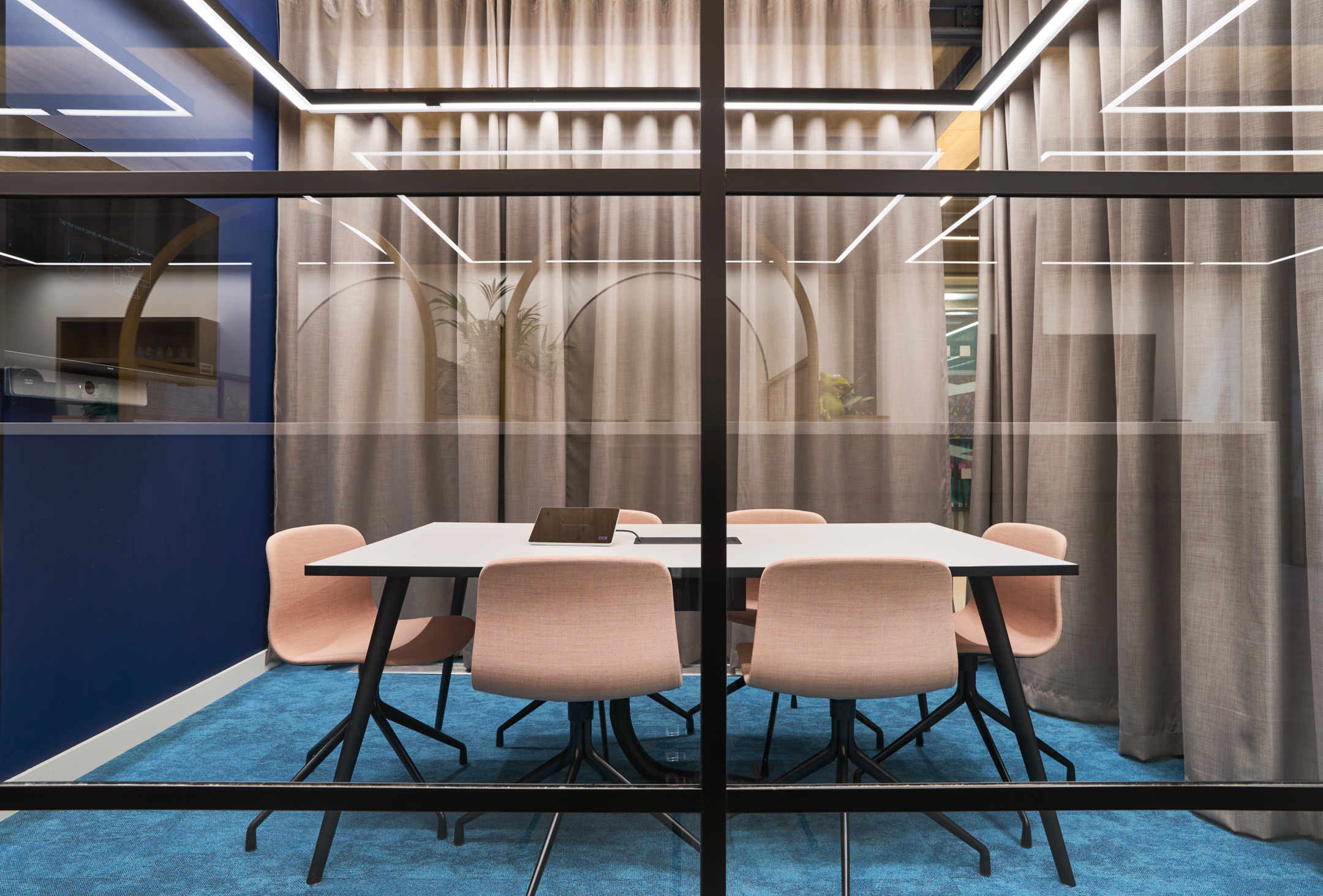 Meeting room at Nomad Foods featuring a rectangular table with blush pink chairs, blue carpet flooring, and sheer curtains adding softness and acoustic privacy.