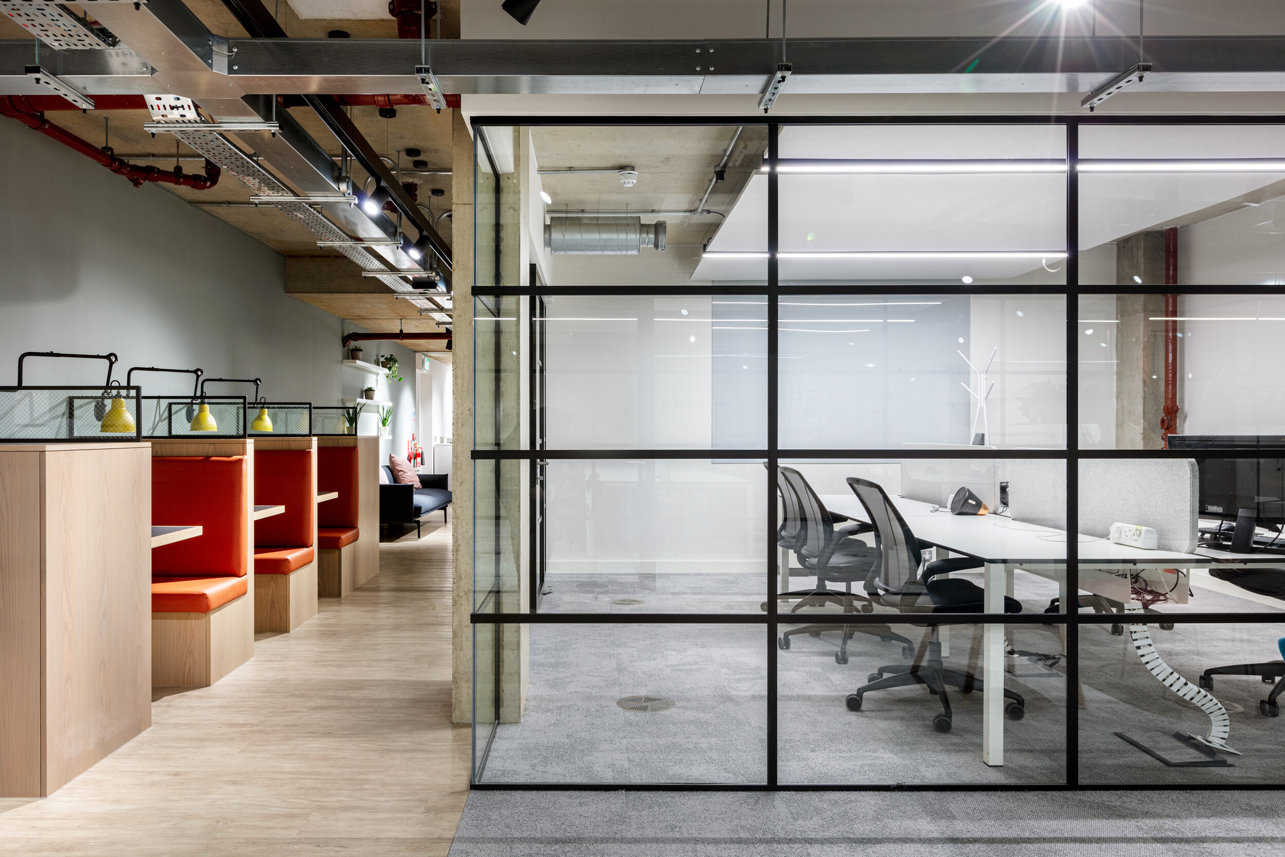 OSE workspace with custom furniture including orange-accented booth seating and ergonomic task chairs in a glazed meeting room.