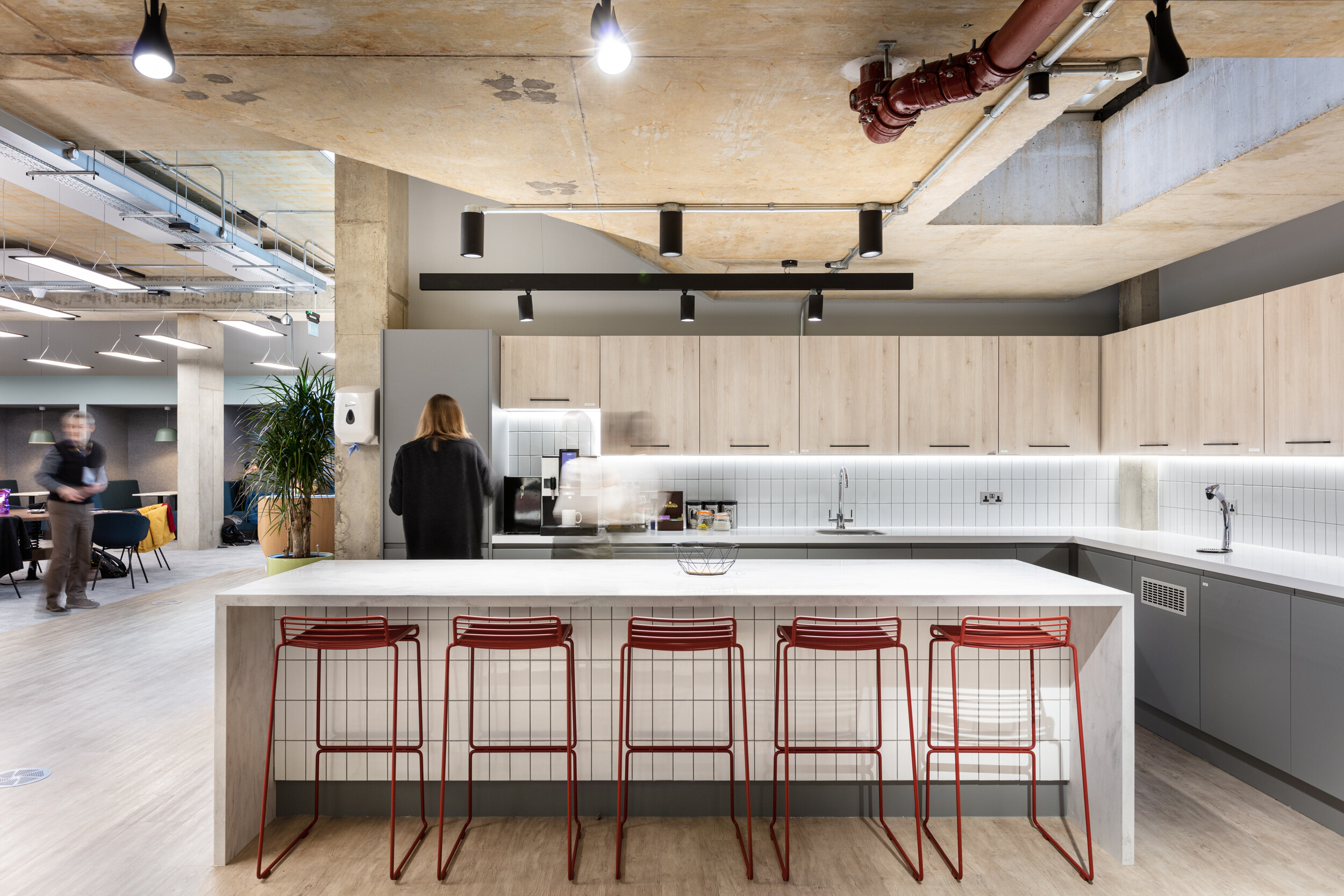OSE office kitchen with modern furniture, including red wireframe bar stools and integrated cabinetry across a bright communal space.