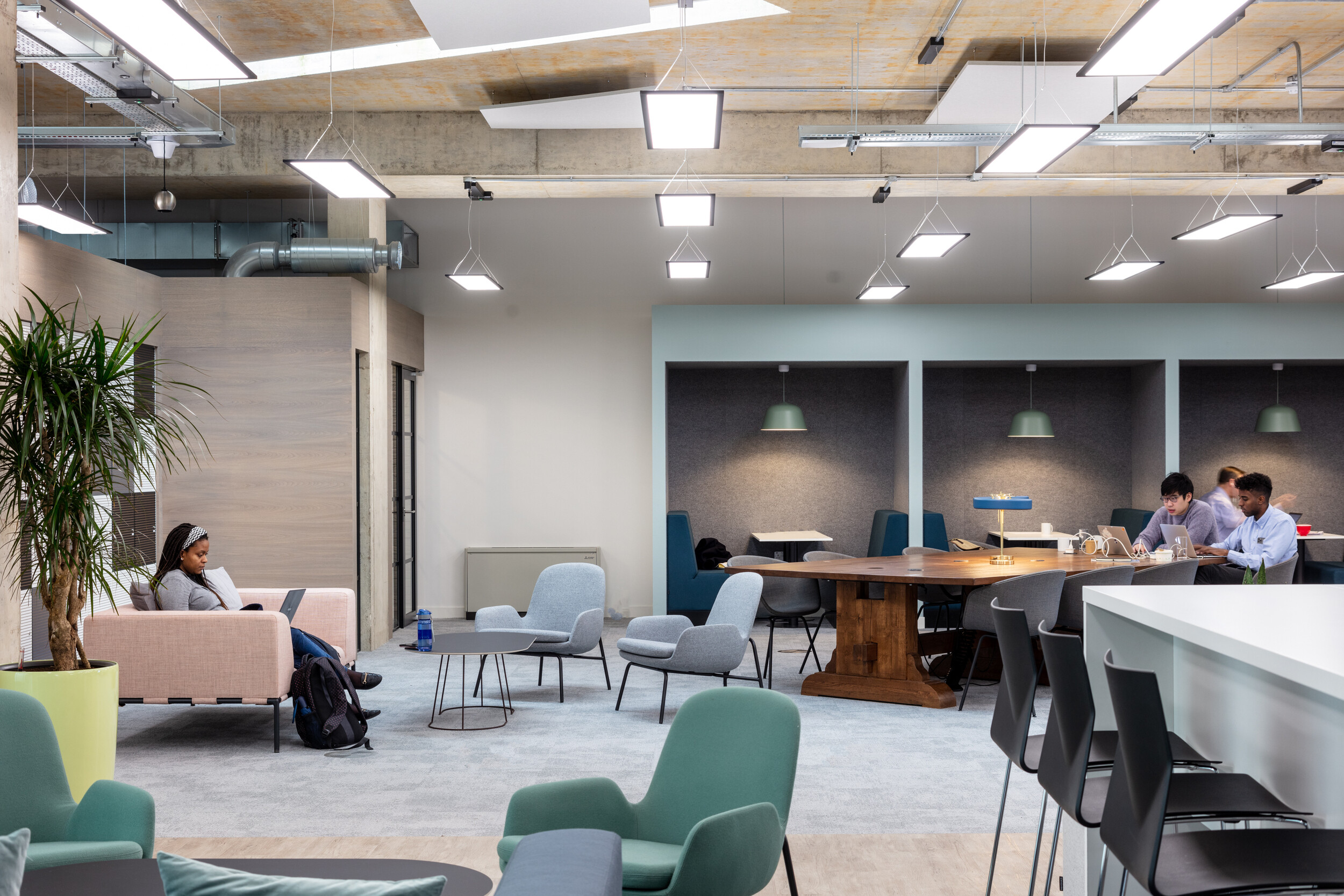 OSE breakout area furnished with soft seating, pastel booths, and a central wooden collaboration table designed for flexible working styles.