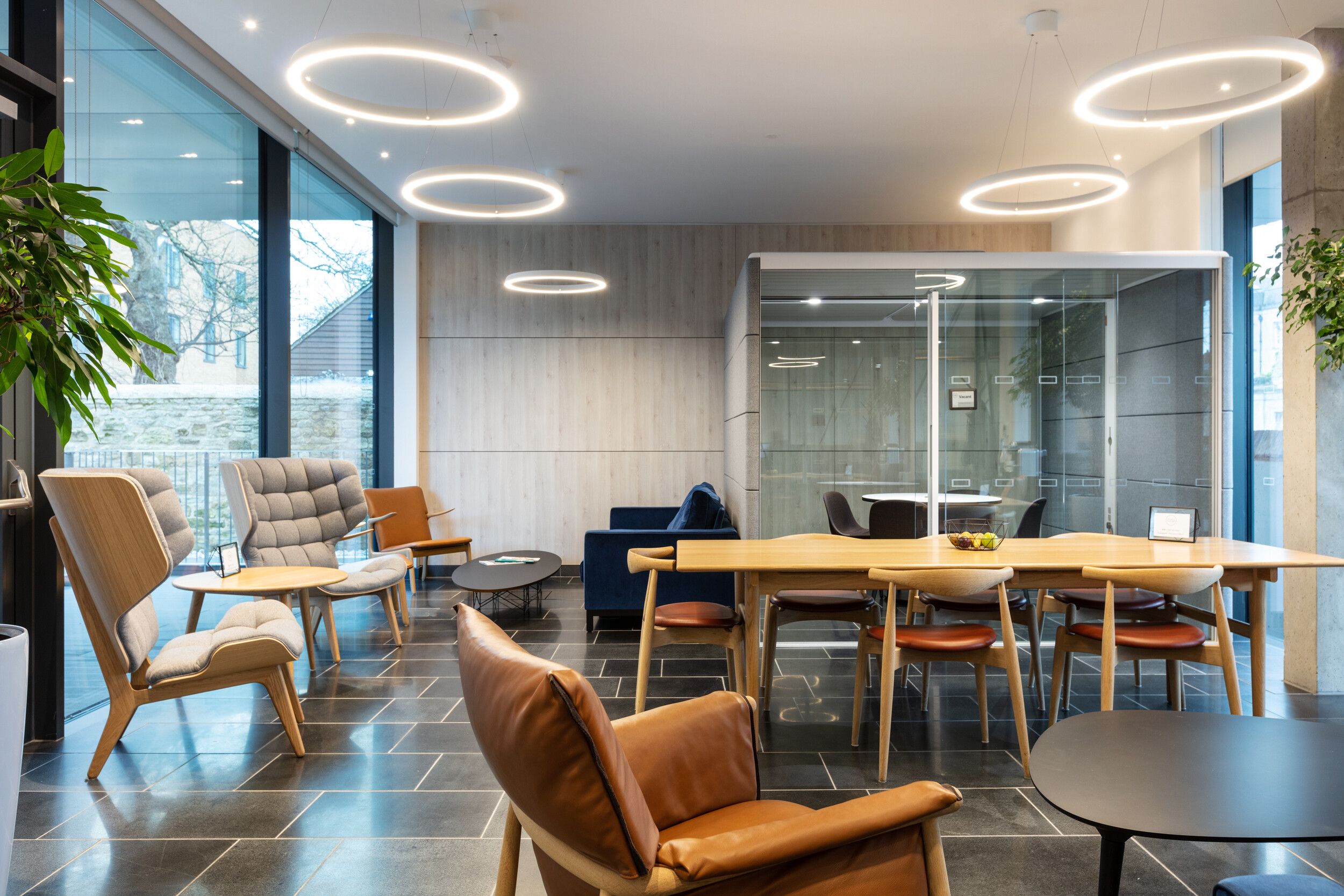 OSE lounge and meeting area with mid-century inspired furniture, including tan leather chairs and a timber table, adjacent to a glazed meeting pod.