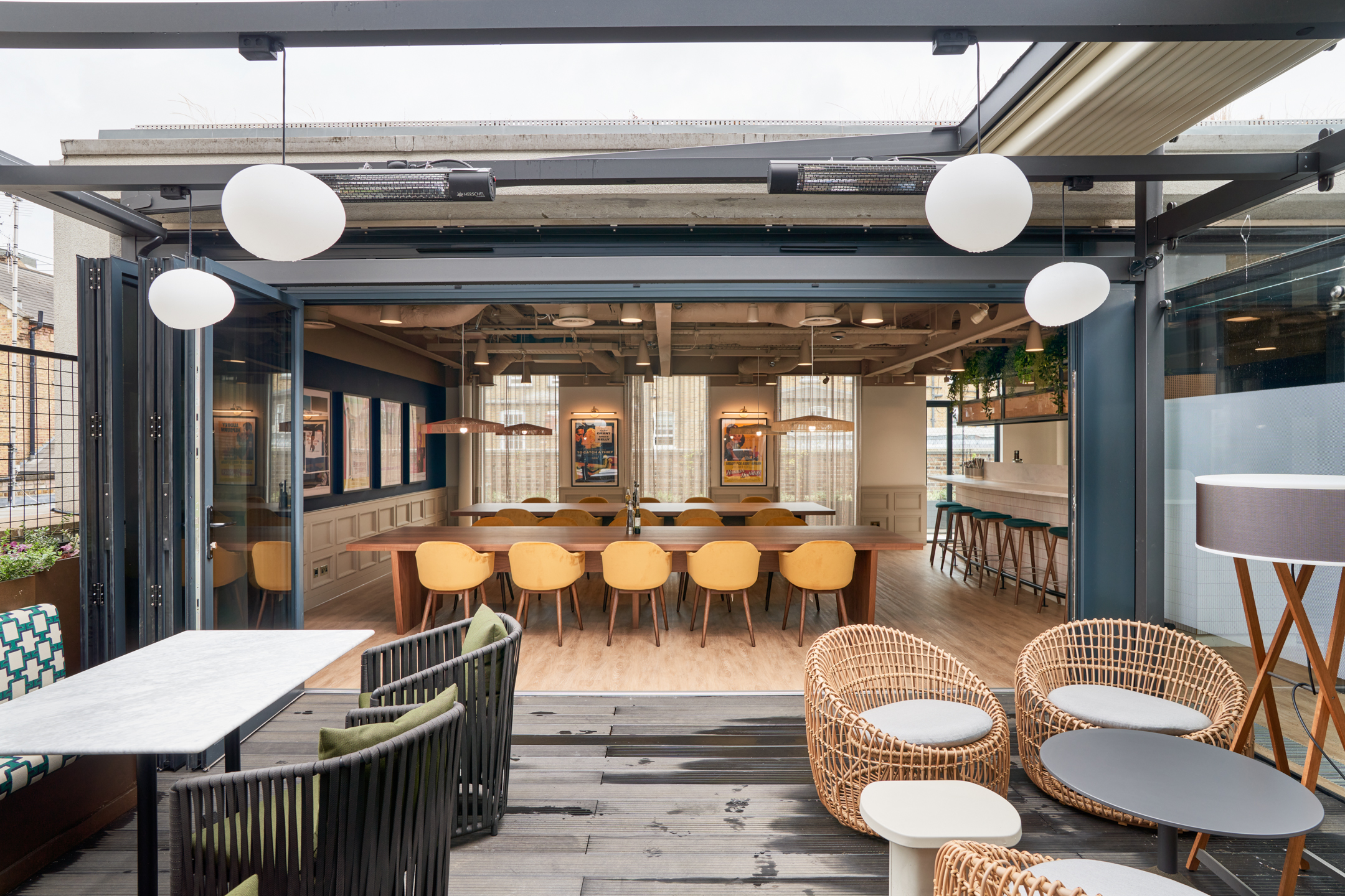 Flexible indoor-outdoor workspace at Private Equity Fund, featuring woven lounge seating, yellow dining chairs, and large communal tables for relaxed meetings.