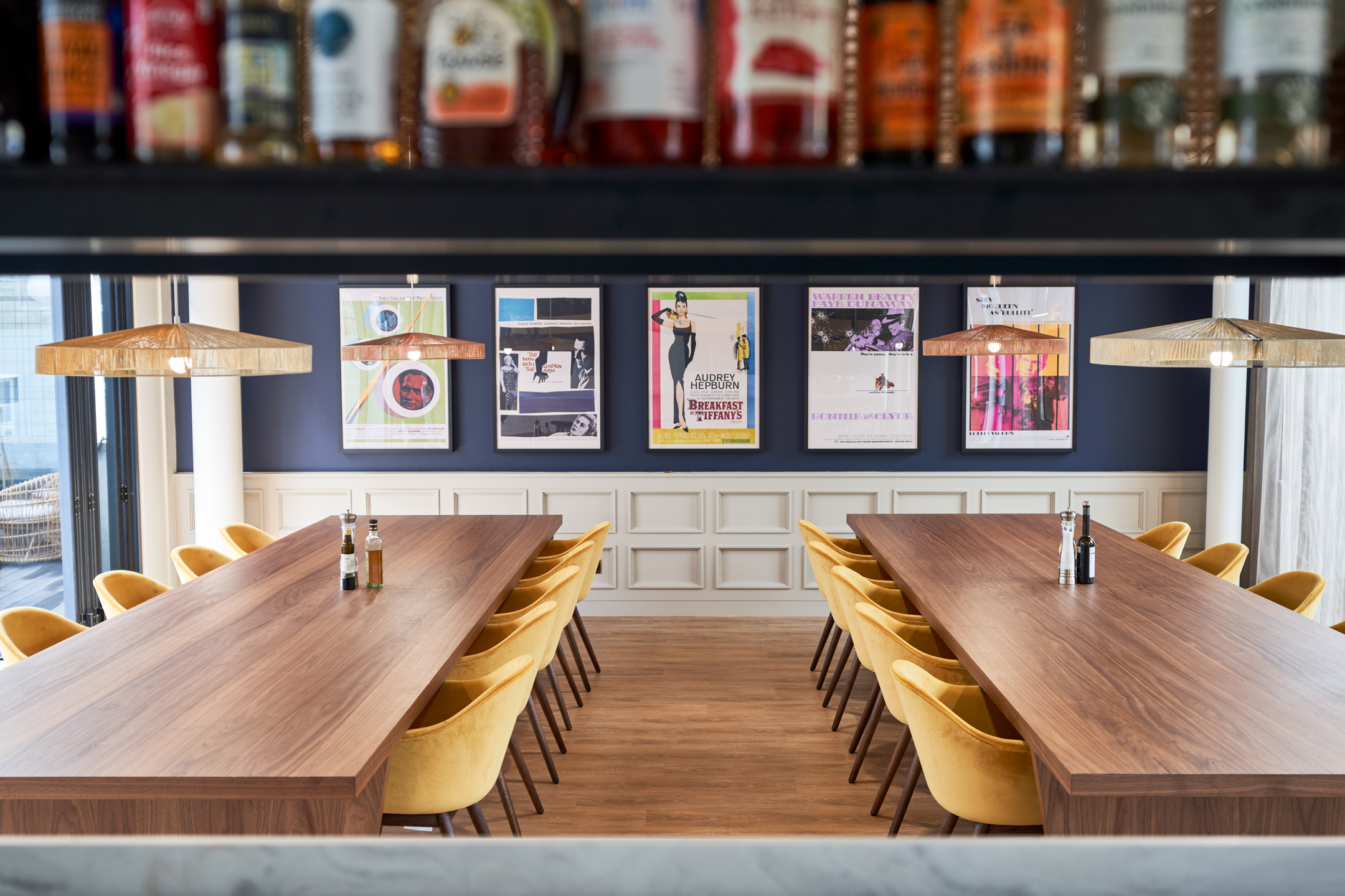 Elegant dining and meeting area at Private Equity Fund, with long walnut tables, yellow velvet chairs, and a gallery wall of vintage film posters.