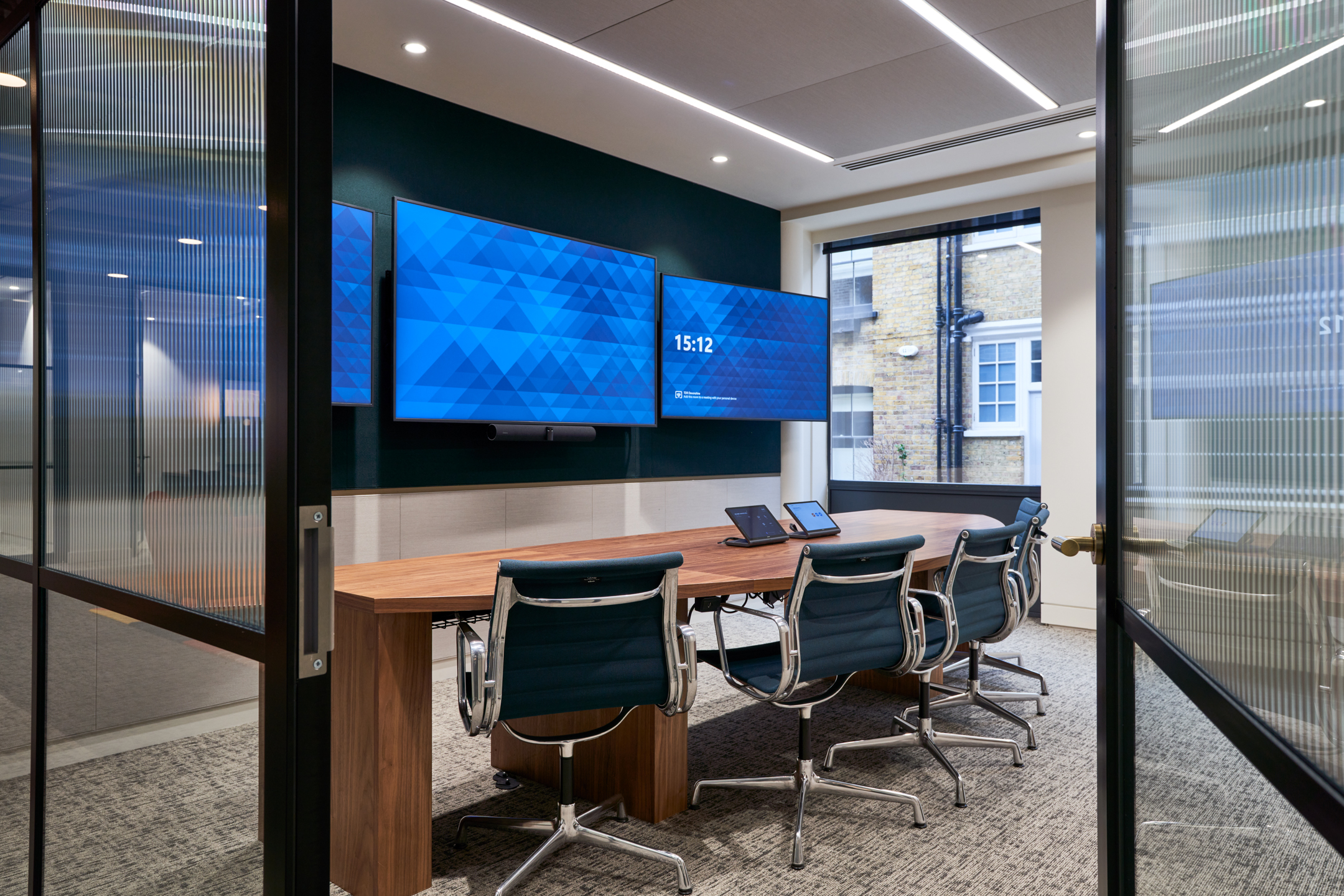 Modern meeting room at Private Equity Fund with triple screen setup, walnut table and ergonomic task chairs designed for high-performance video conferencing.