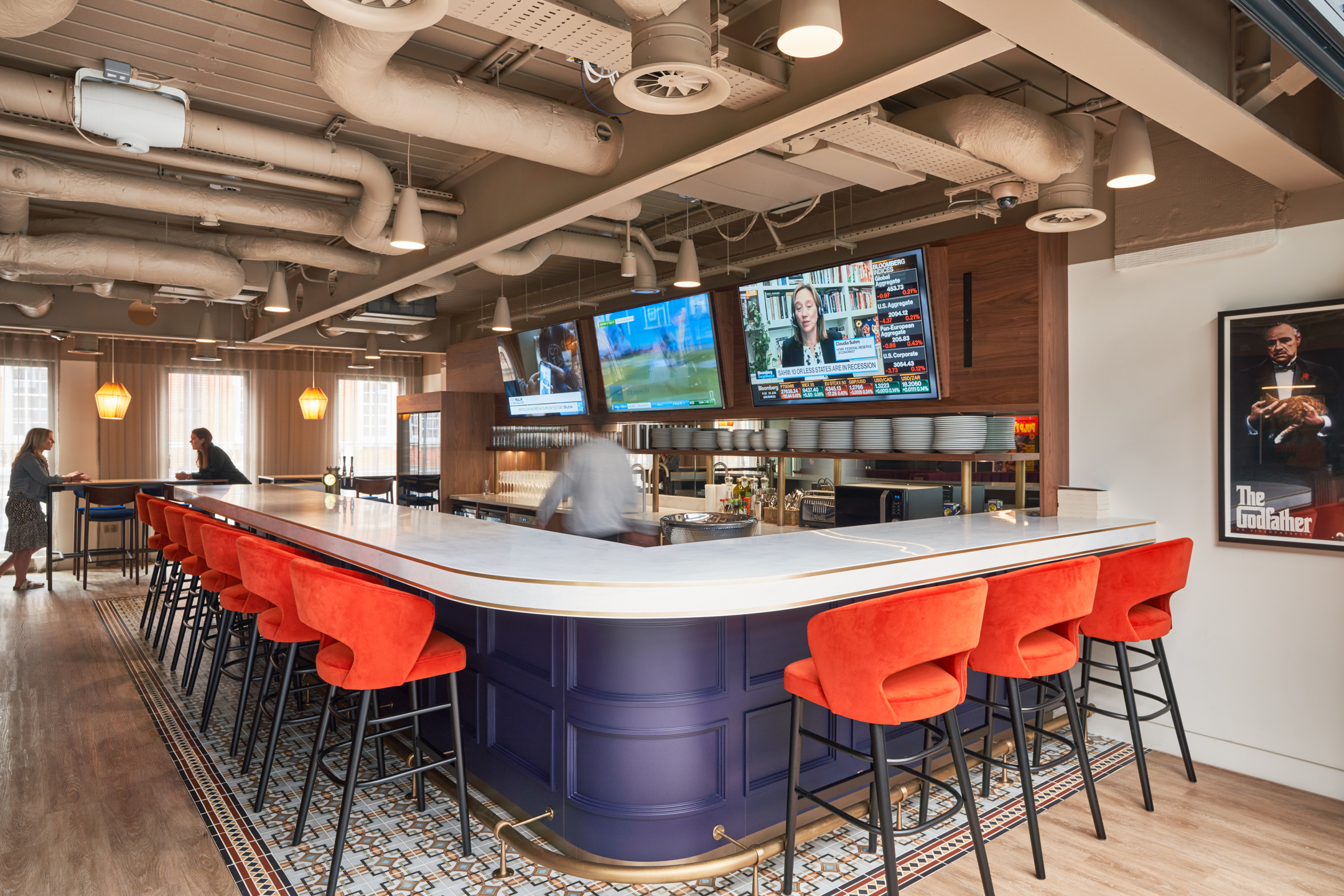 Lively bar at Private Equity Fund, complete with bold red stools, dark blue panelling, and mounted screens for a social, hospitality-style setting.