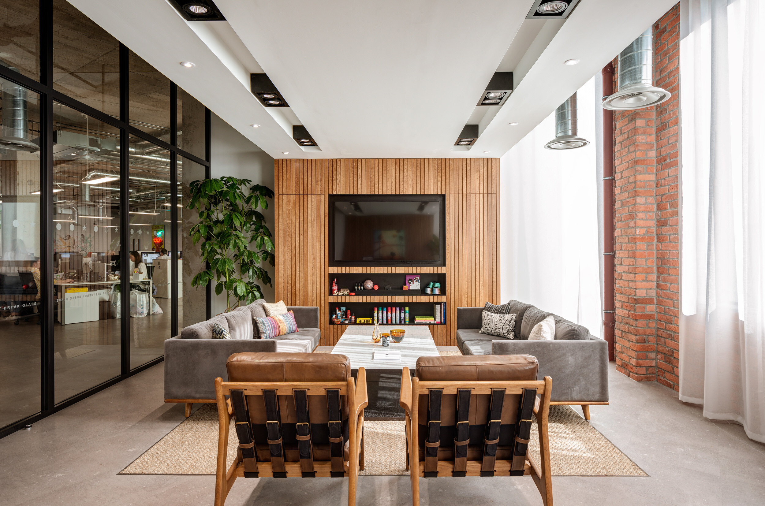SLG’s Cheltenham office lounge with sofas, leather armchairs and a timber media wall, furnished to support informal meetings and downtime.
