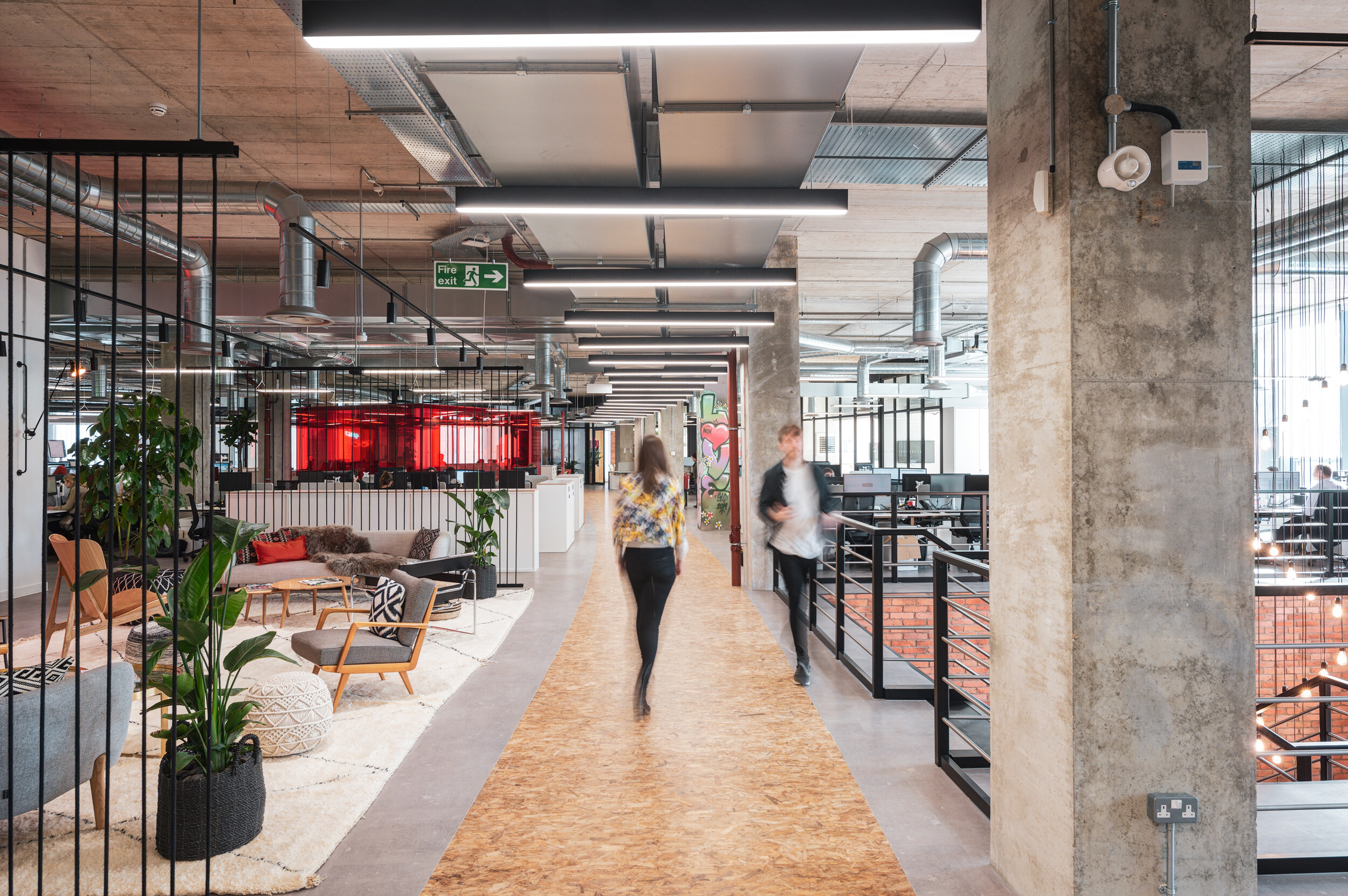 SLG office in Cheltenham with open-plan zones and breakout furniture, including soft seating and lounge chairs placed along the central walkway.