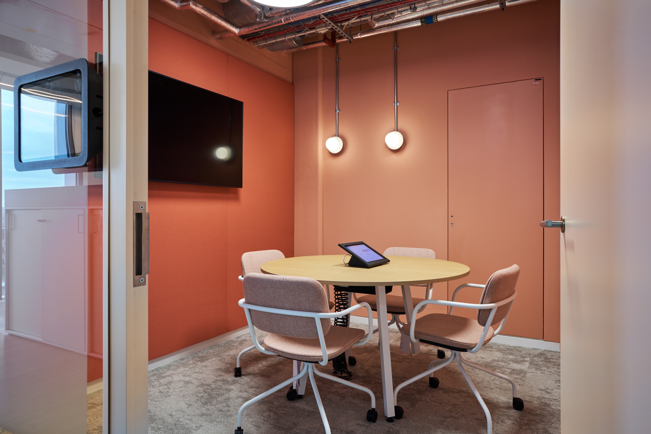 Salesloft meeting pod with coral-toned walls, round oak table and soft pink chairs, furnished by Platfform for intimate, tech-ready collaboration.