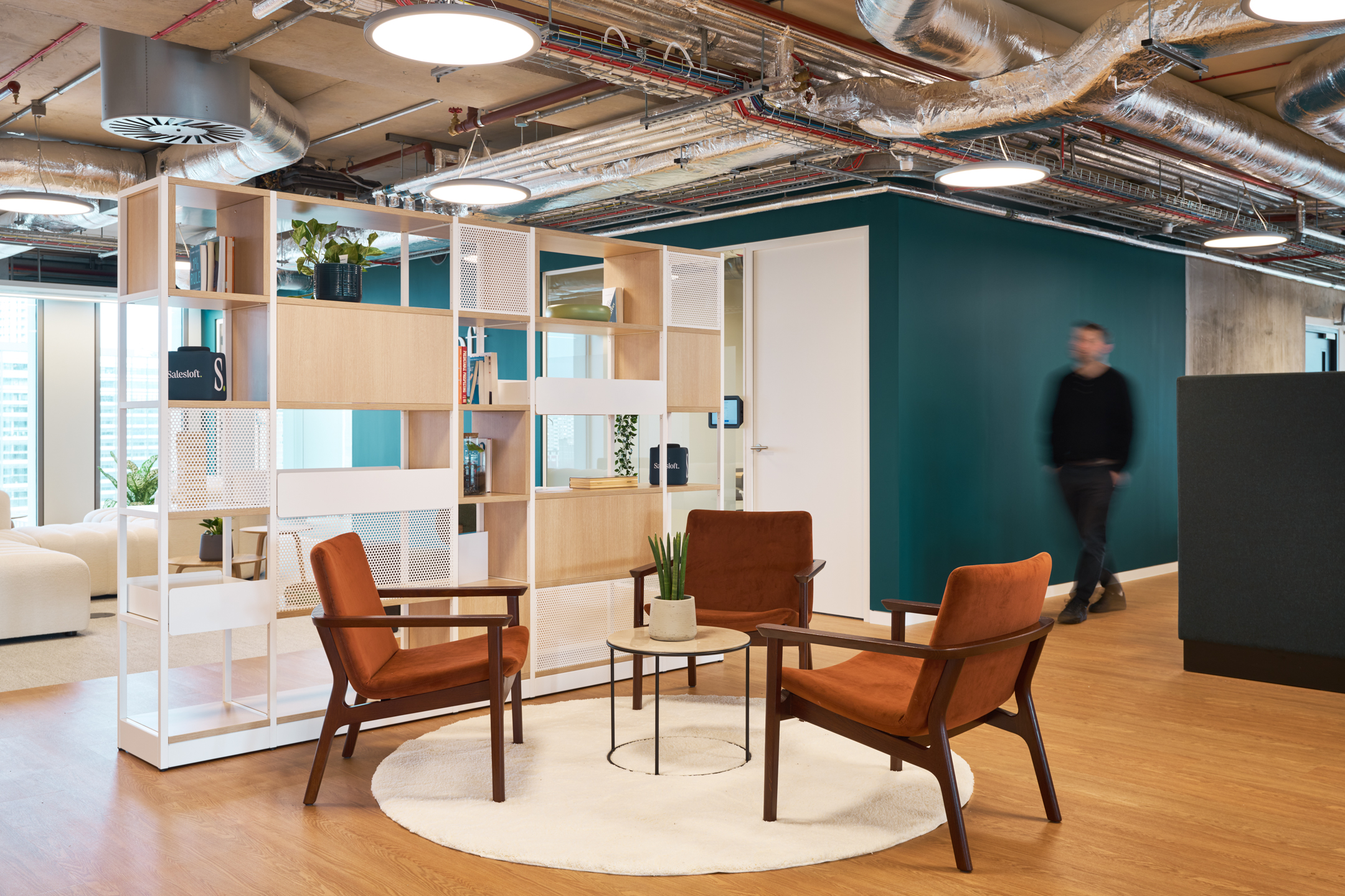 Salesloft informal meeting area with burnt orange lounge chairs and a circular rug, furnished by Platfform and framed by an open shelving divider.