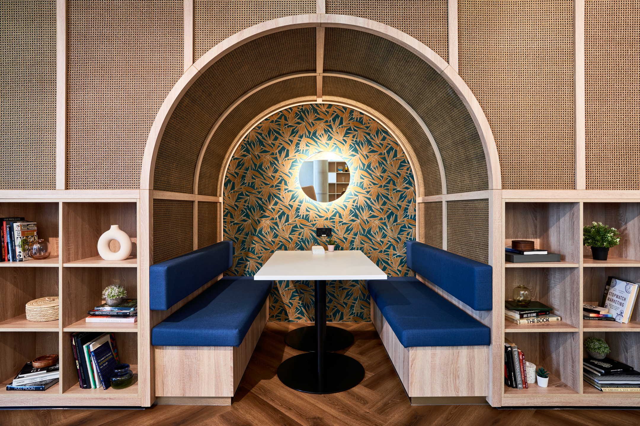 Close-up of a meeting booth at Publicis Sapient, furnished by Platfform with blue upholstered seating, rattan panelling and leafy print wallpaper.