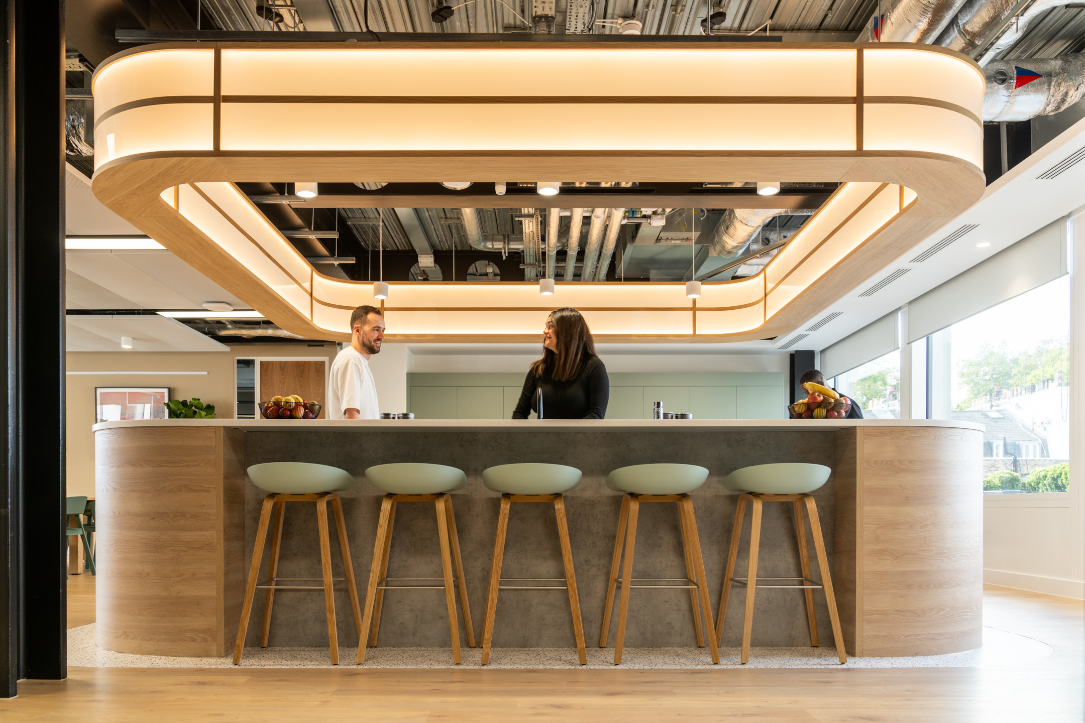 Shionogi’s workplace teapoint with curved wood panelling, Japandi-style bar stools and soft lighting designed for calm and informal conversation.