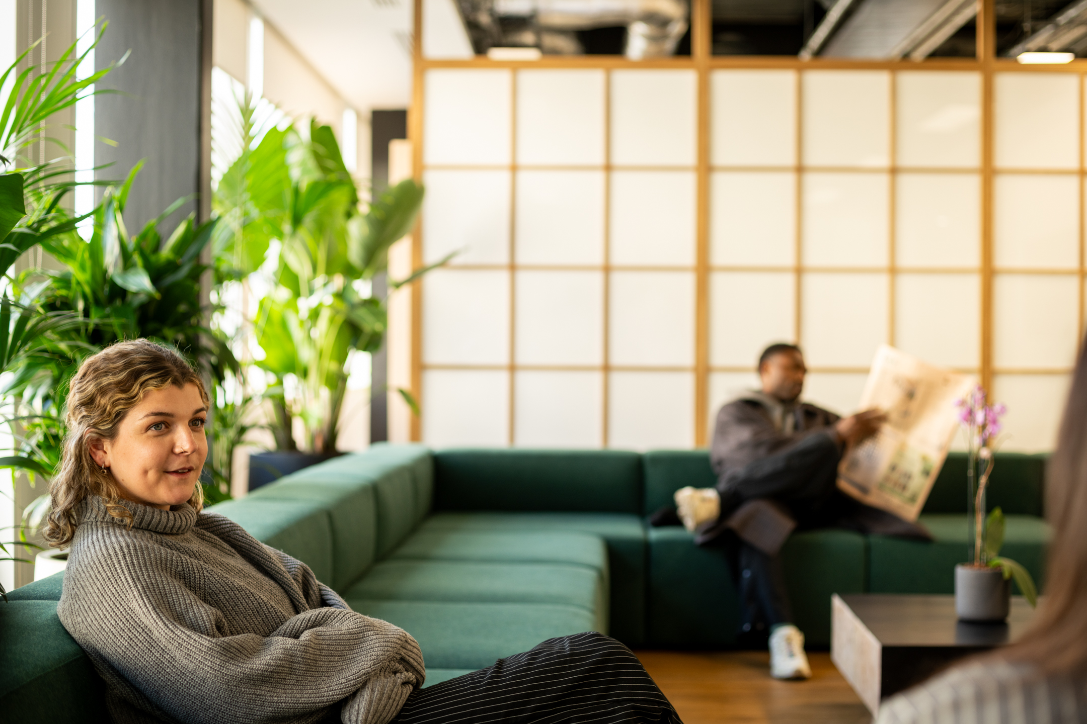 Shionogi breakout space with green modular sofa and a Japandi-style screen backdrop, styled with soft lines and greenery for a calm, layered feel.