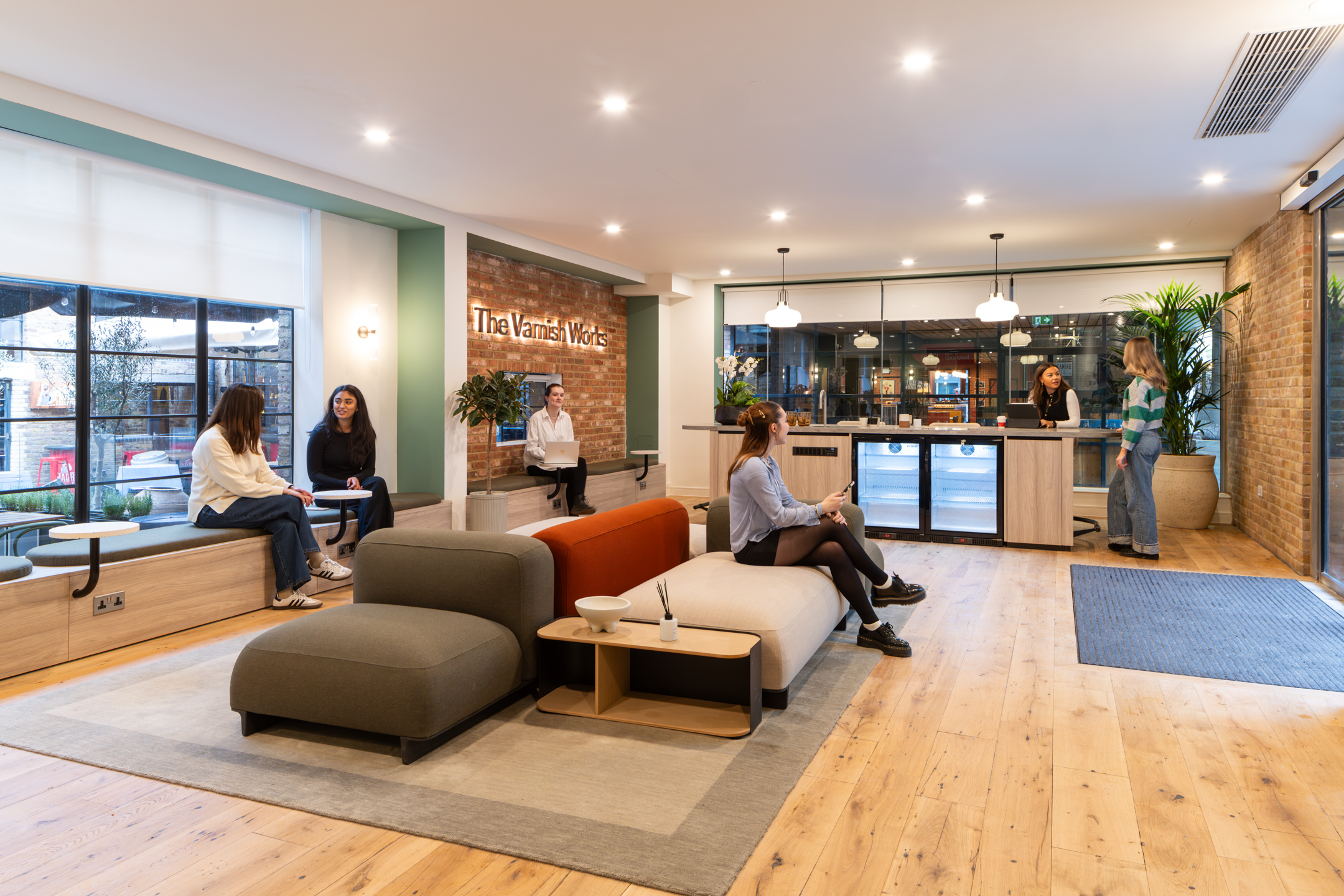 Layered furniture at The Varnish Works with soft textures, warm tones, and bold shapes set against exposed brick and heritage-style windows