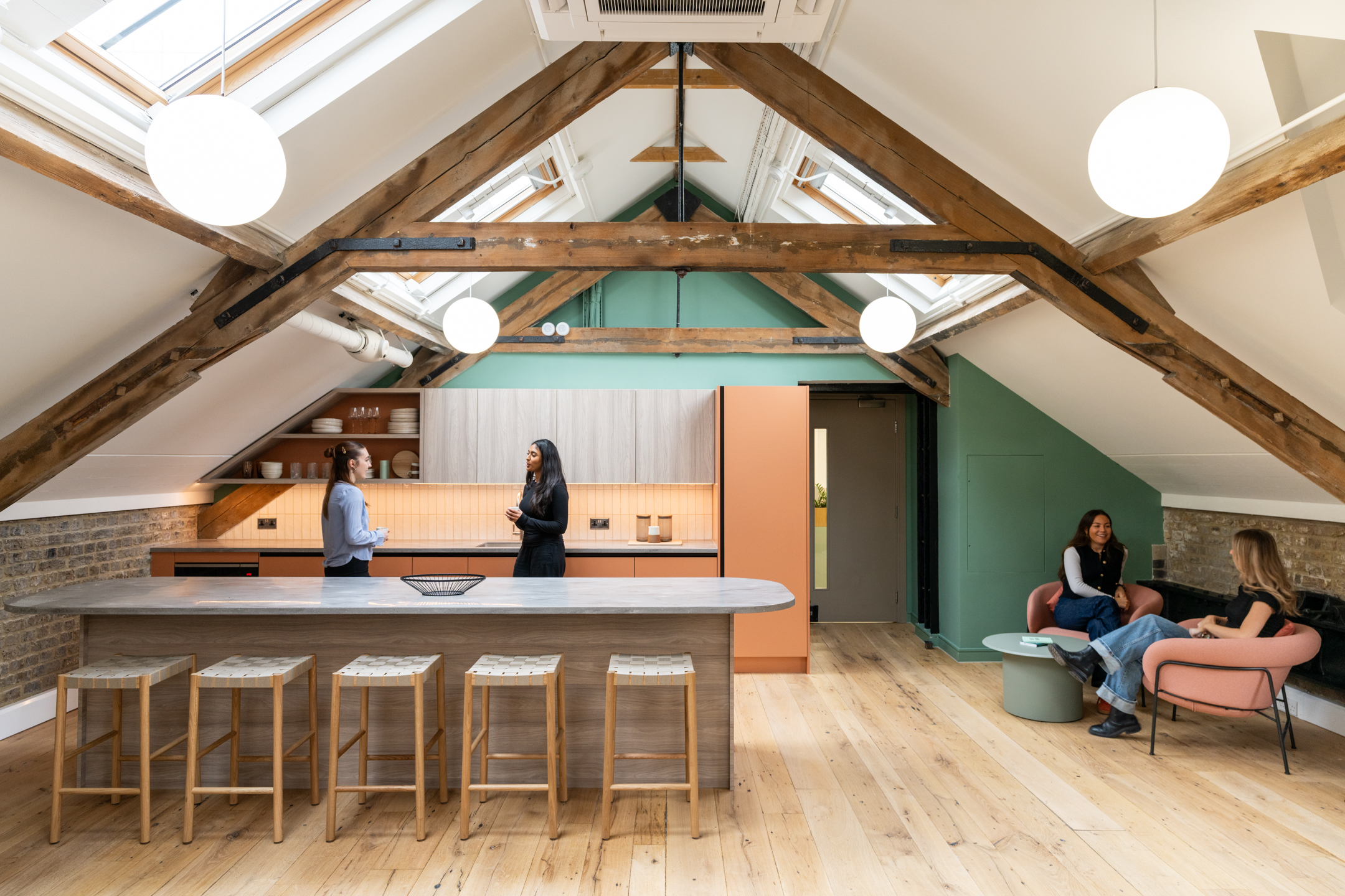 Textured stools and soft blush seating add warmth to the loft kitchen space at The Varnish Works under exposed beams and skylight-filled ceilings