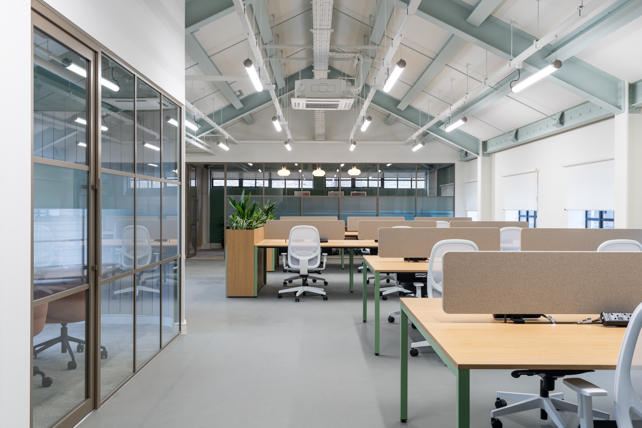 Clean-lined desks and ergonomic chairs define the open workspace at The Varnish Works, framed by powder-coated steel and pitched roof beams