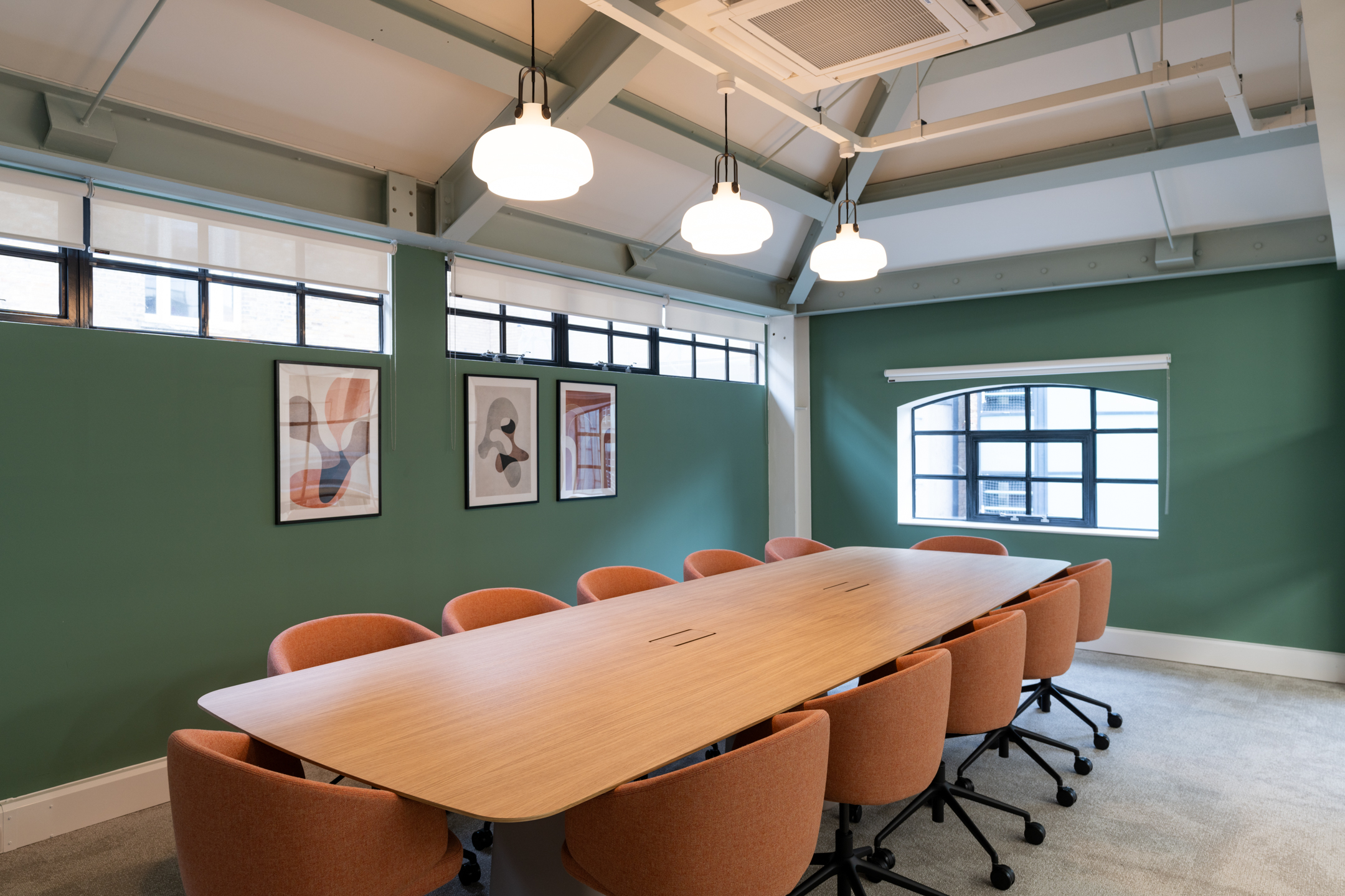 Terracotta chairs and a pale wood table give the meeting room at The Varnish Works a warm, modern edge against sage walls and steel-framed windows