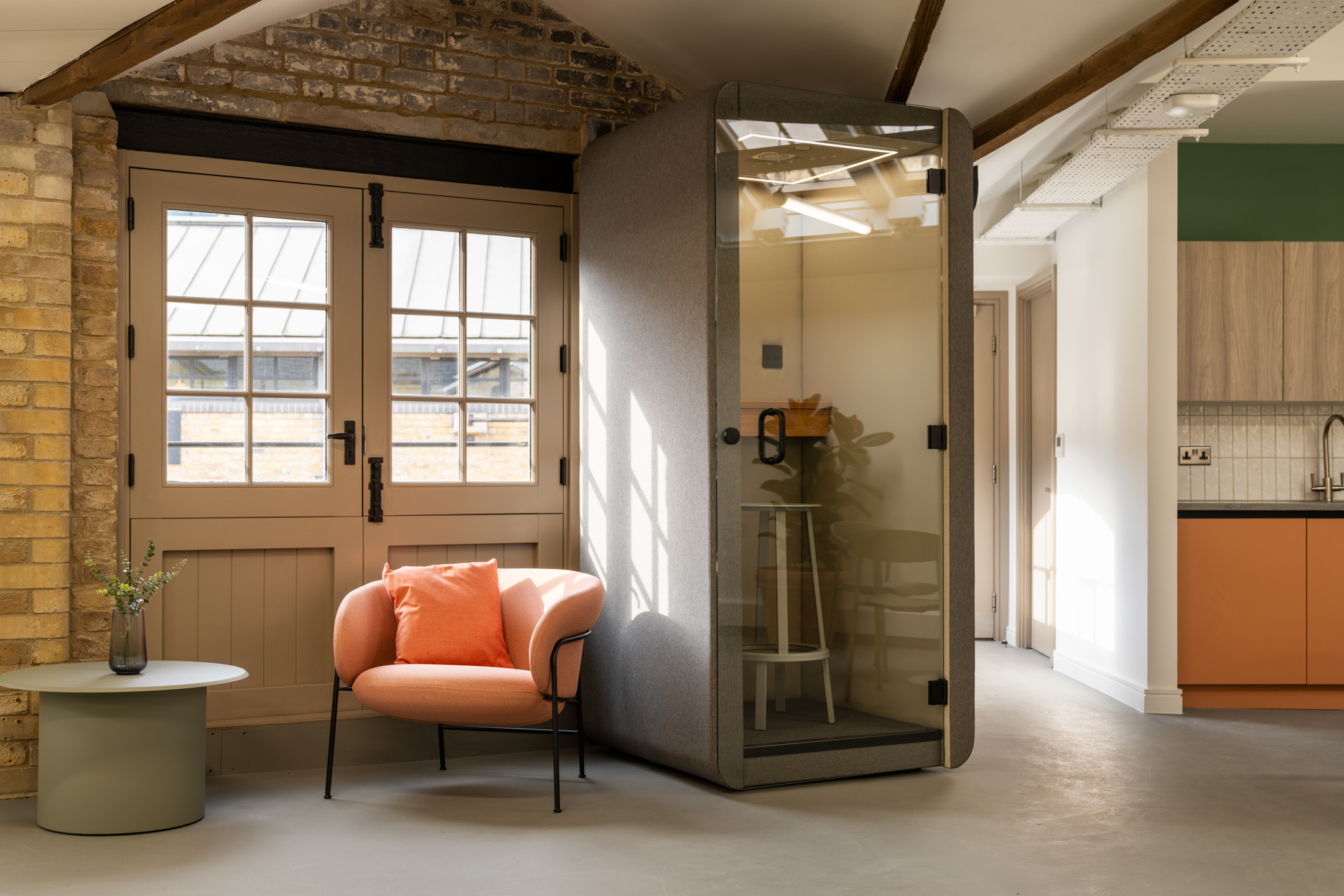Private booth and coral lounge chair sit under rustic beams at The Varnish Works, styled with soft light, heritage doors and warm-toned joinery