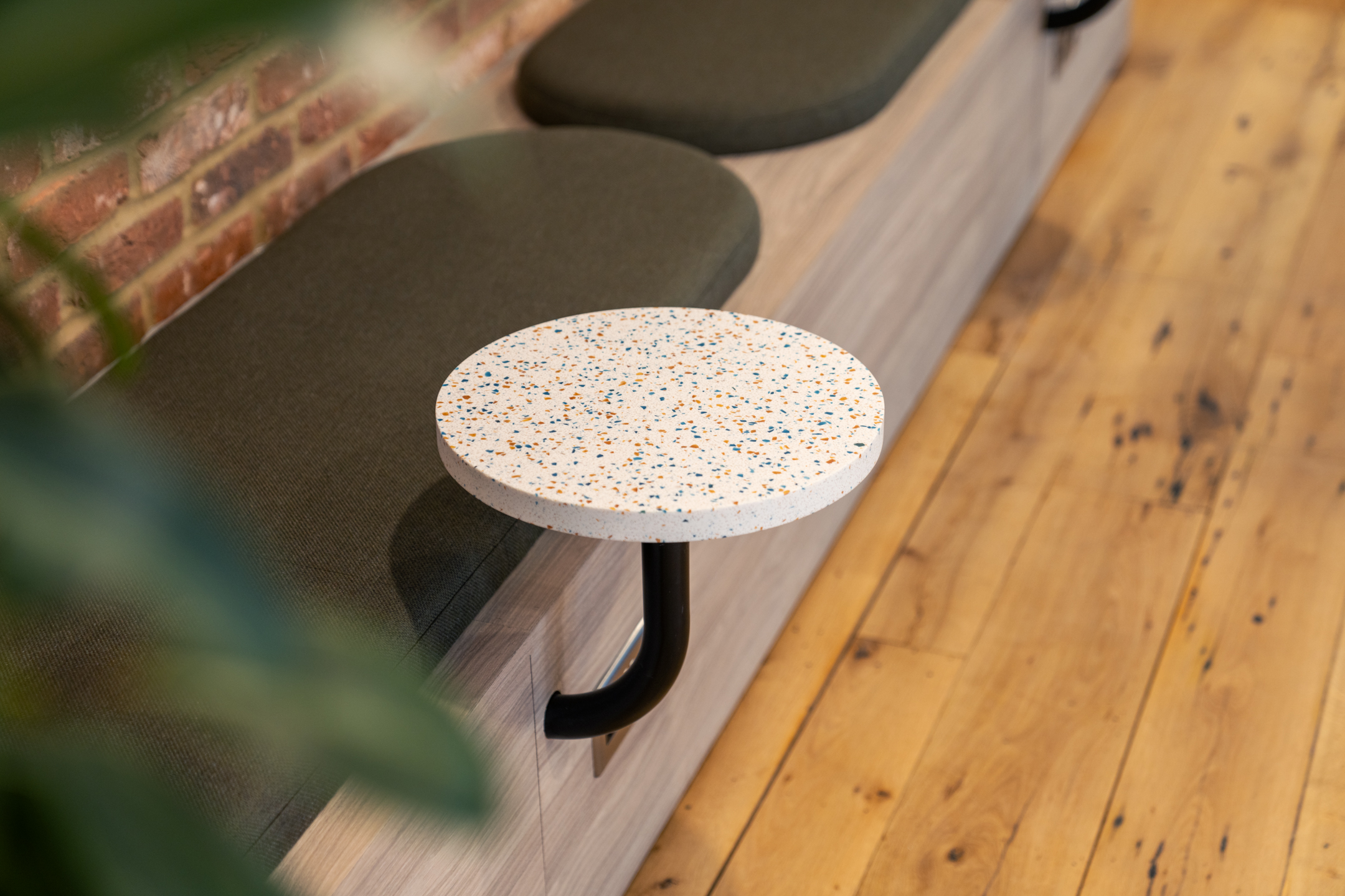 Close-up of terrazzo table and bench cushions at The Varnish Works, styled with deep green upholstery and set against aged timber flooring