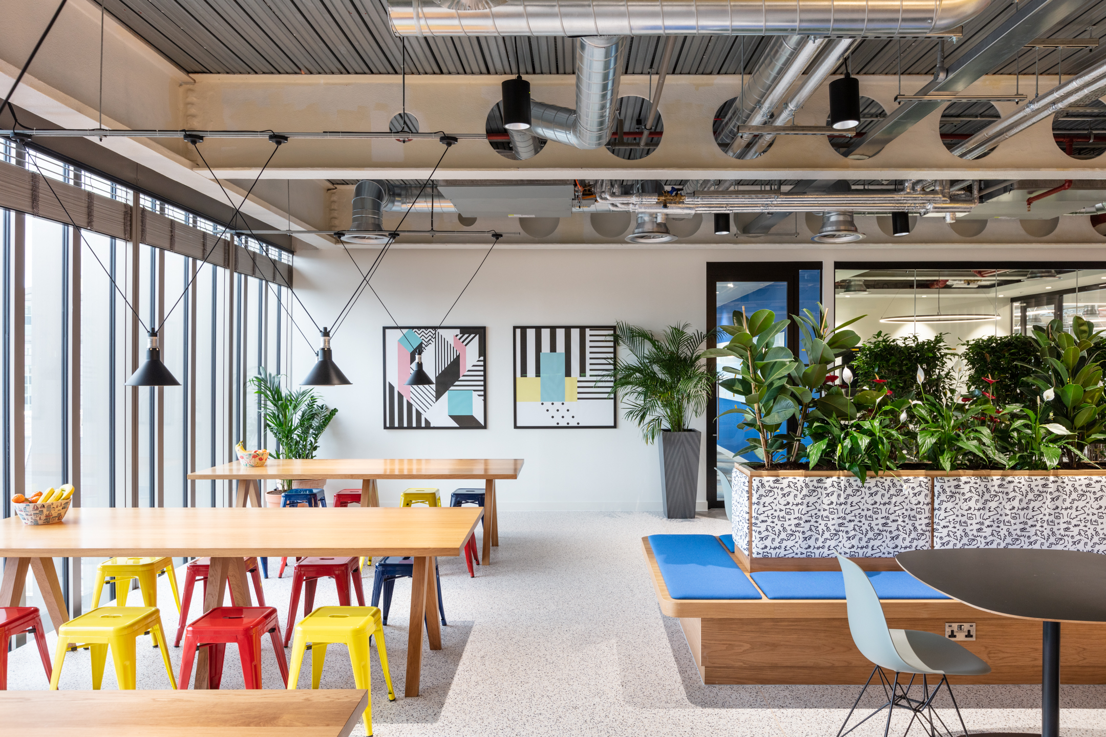Travelfusion dining space with Platfform-supplied communal tables, colourful stools and integrated planters that connect social zones with soft seating.