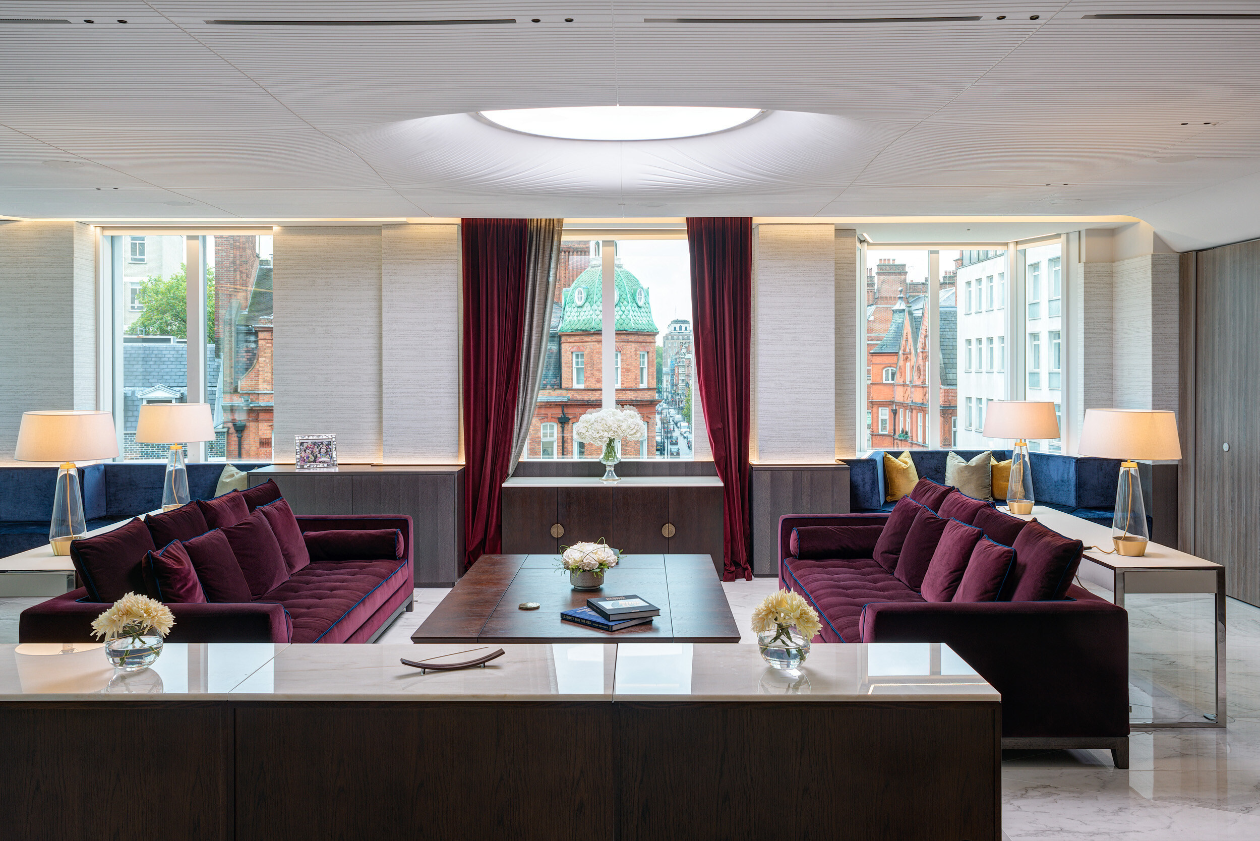 Lounge setting in Vedanta’s London office with burgundy sofas, marble-topped consoles and city views, combining elegance with soft residential tones.