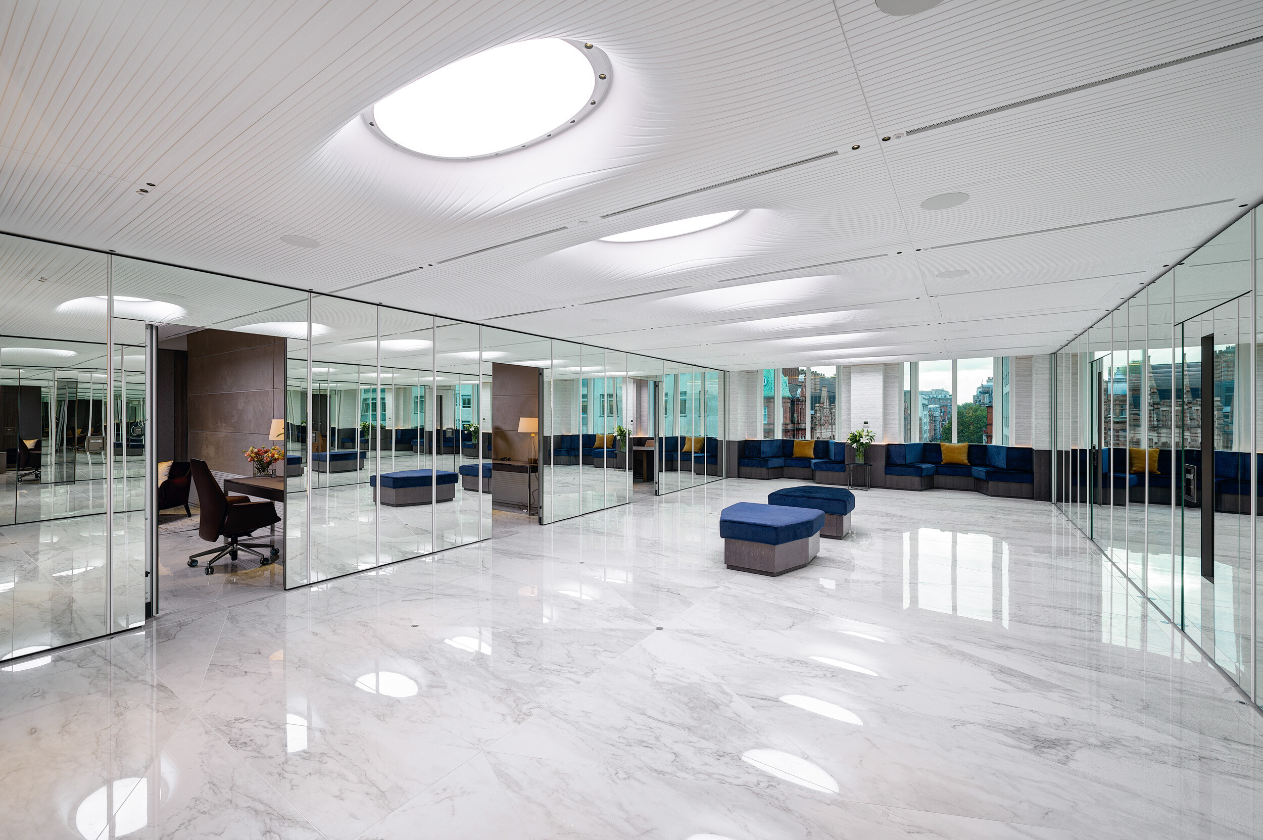 Open-plan breakout area at Vedanta’s London office with mirrored walls, marble flooring and modular soft seating in rich navy and gold accents.