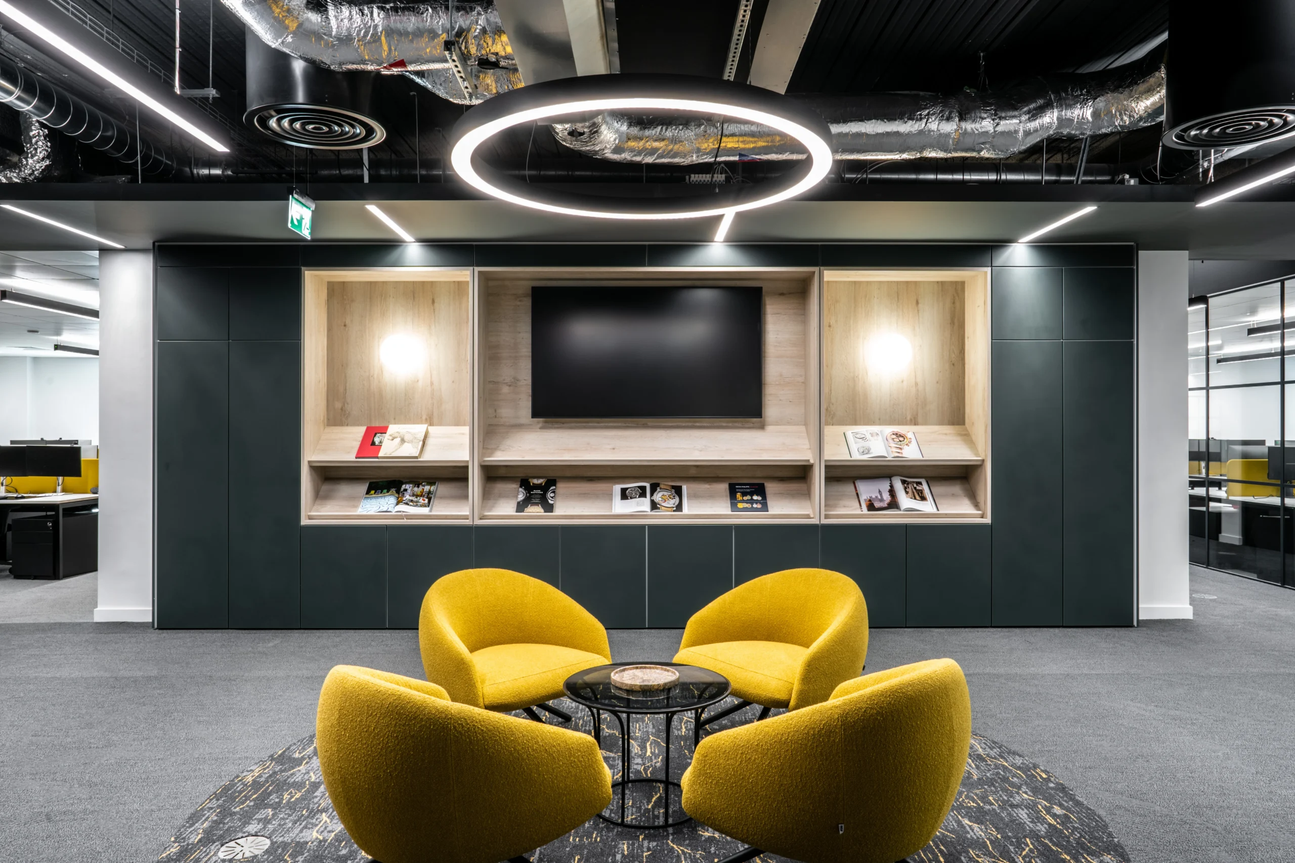 Reading zone at Watches of Switzerland with yellow lounge chairs, open shelving for magazines, and a central screen beneath halo lighting
