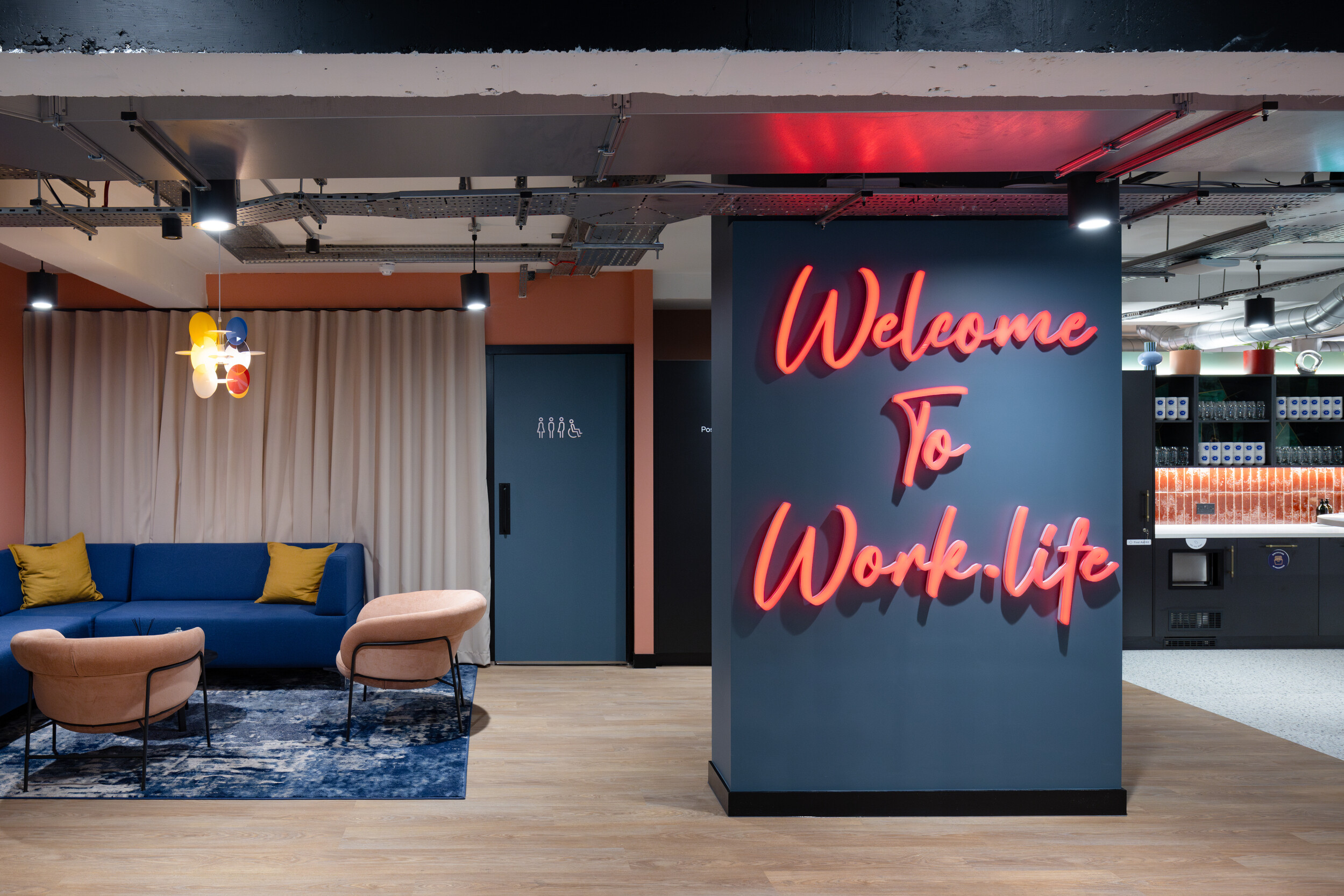 Bold welcome signage and soft-toned furniture in the lounge area at Work.Life Courtyard Building, featuring peach chairs and a deep blue sofa.