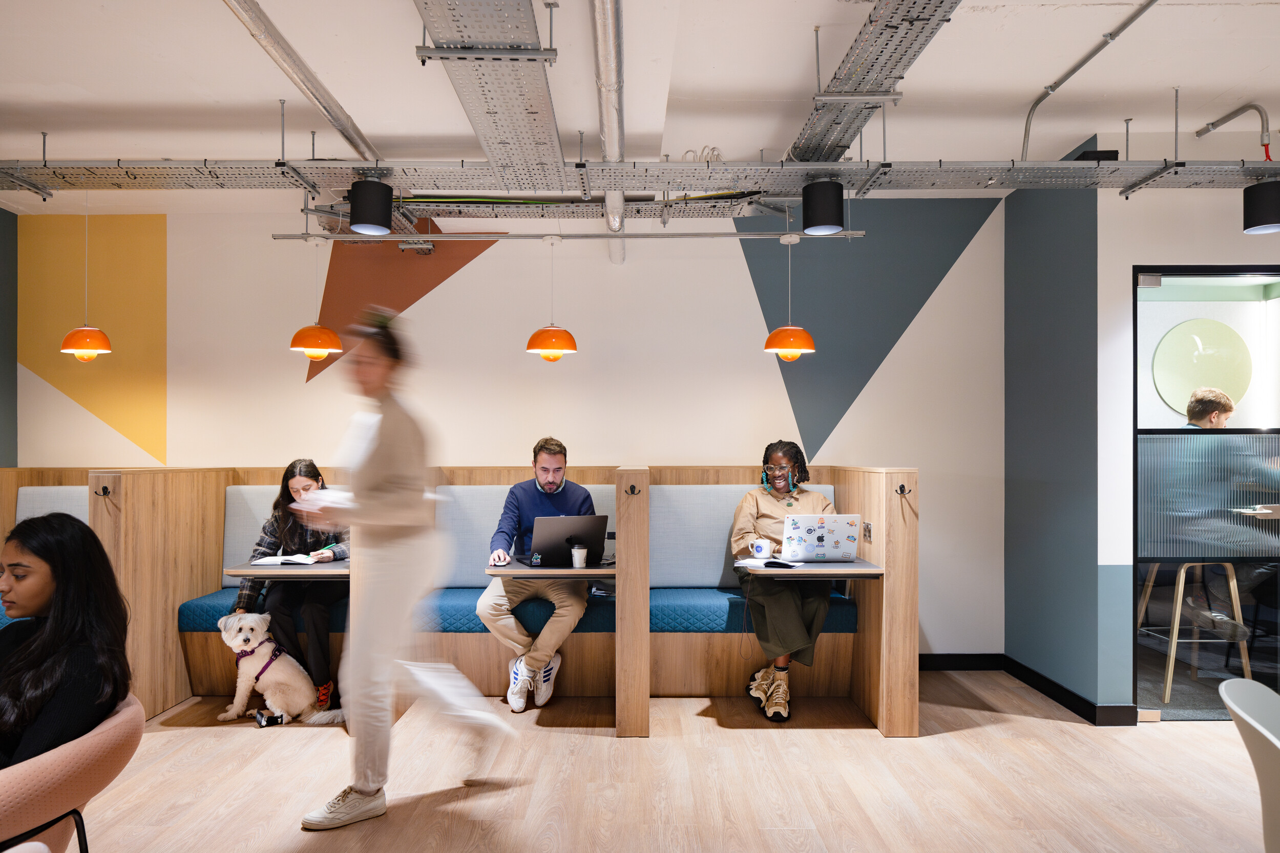 Booth seating at Work.Life Courtyard Building with soft blue upholstery, wooden surrounds, and playful orange pendant lights in a bright, pet-friendly space.