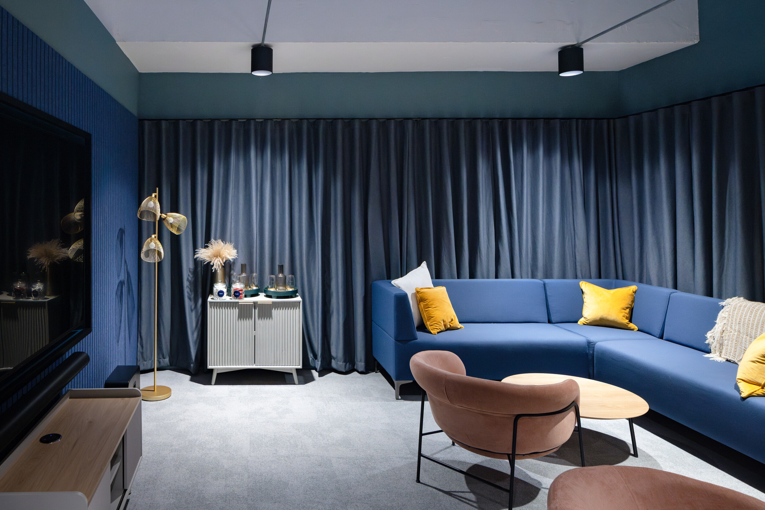 Lounge space at Work.Life Courtyard Building with a deep blue modular sofa, mustard cushions, and soft-toned armchairs set against layered textures.