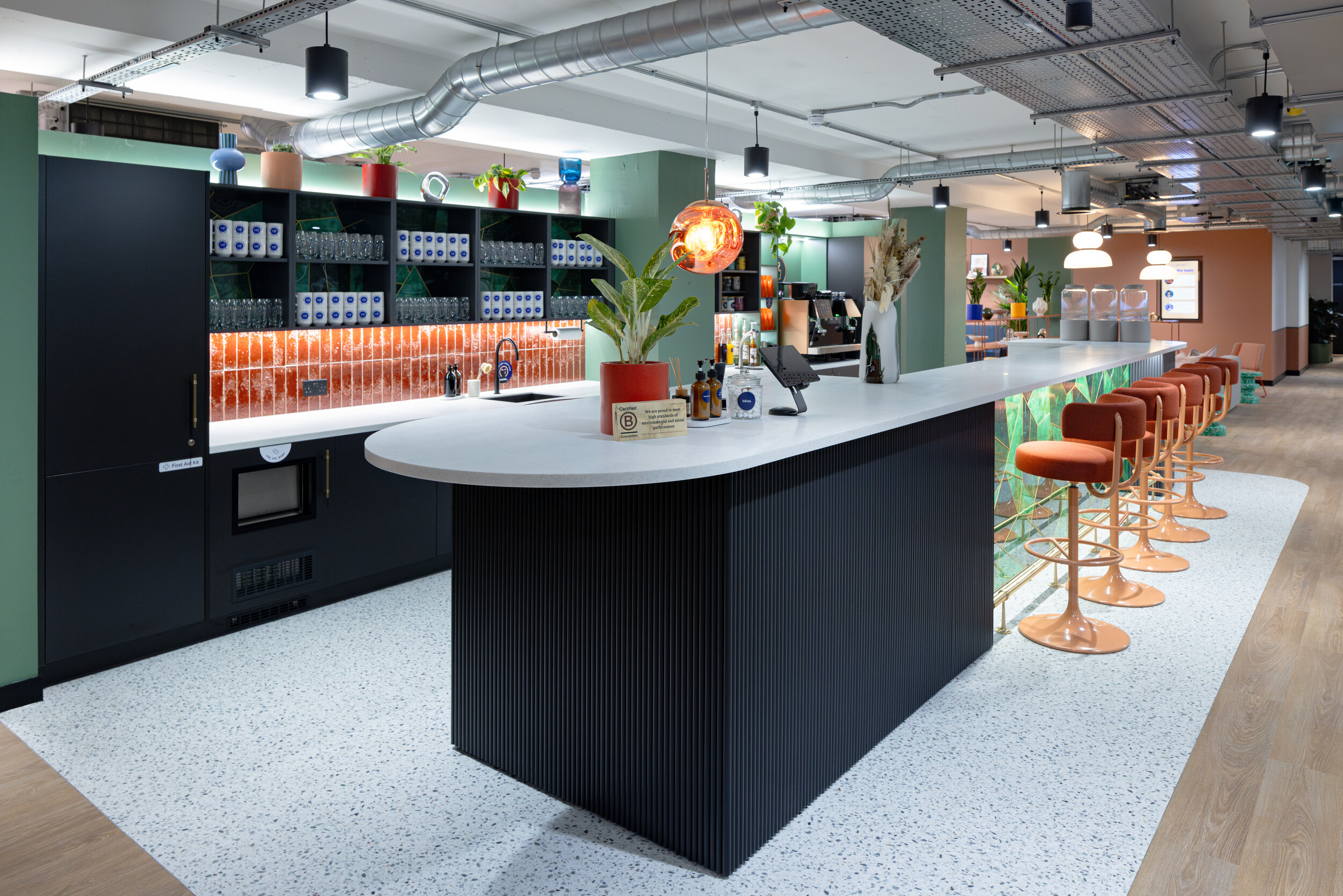 Café-style bar at Work.Life Courtyard Building with orange bar stools, terrazzo flooring, and playful lighting that brings colour and comfort together.