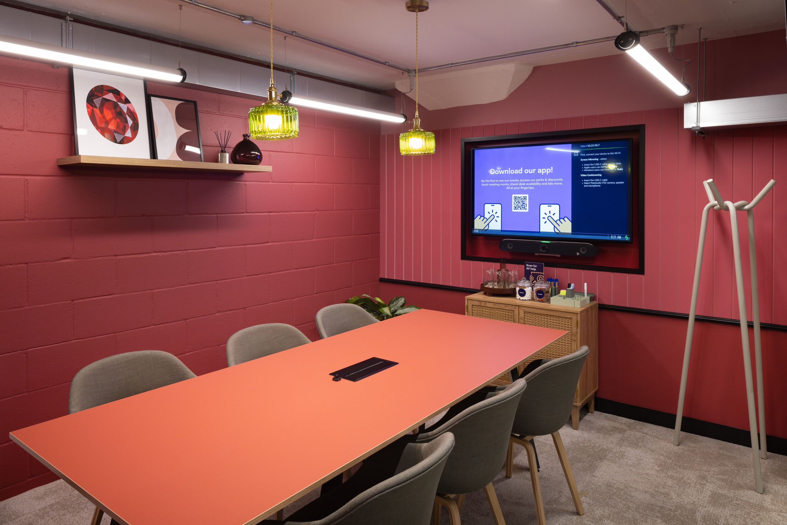 Ruby meeting room at Work.Life Courtyard Building with a coral table, grey upholstered chairs, green glass pendants, and red-toned interior styling.
