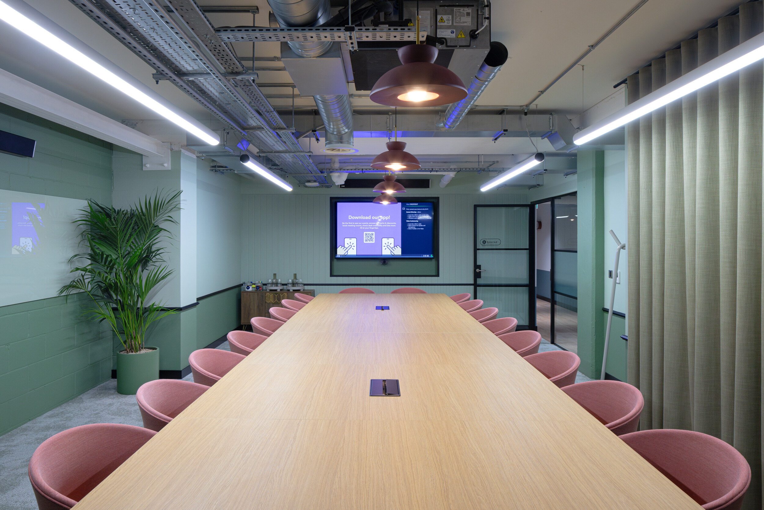 Boardroom at Work.Life Courtyard Building with a long timber table, soft pink chairs, sage green walls, and pendant lighting for a calm, focused space.