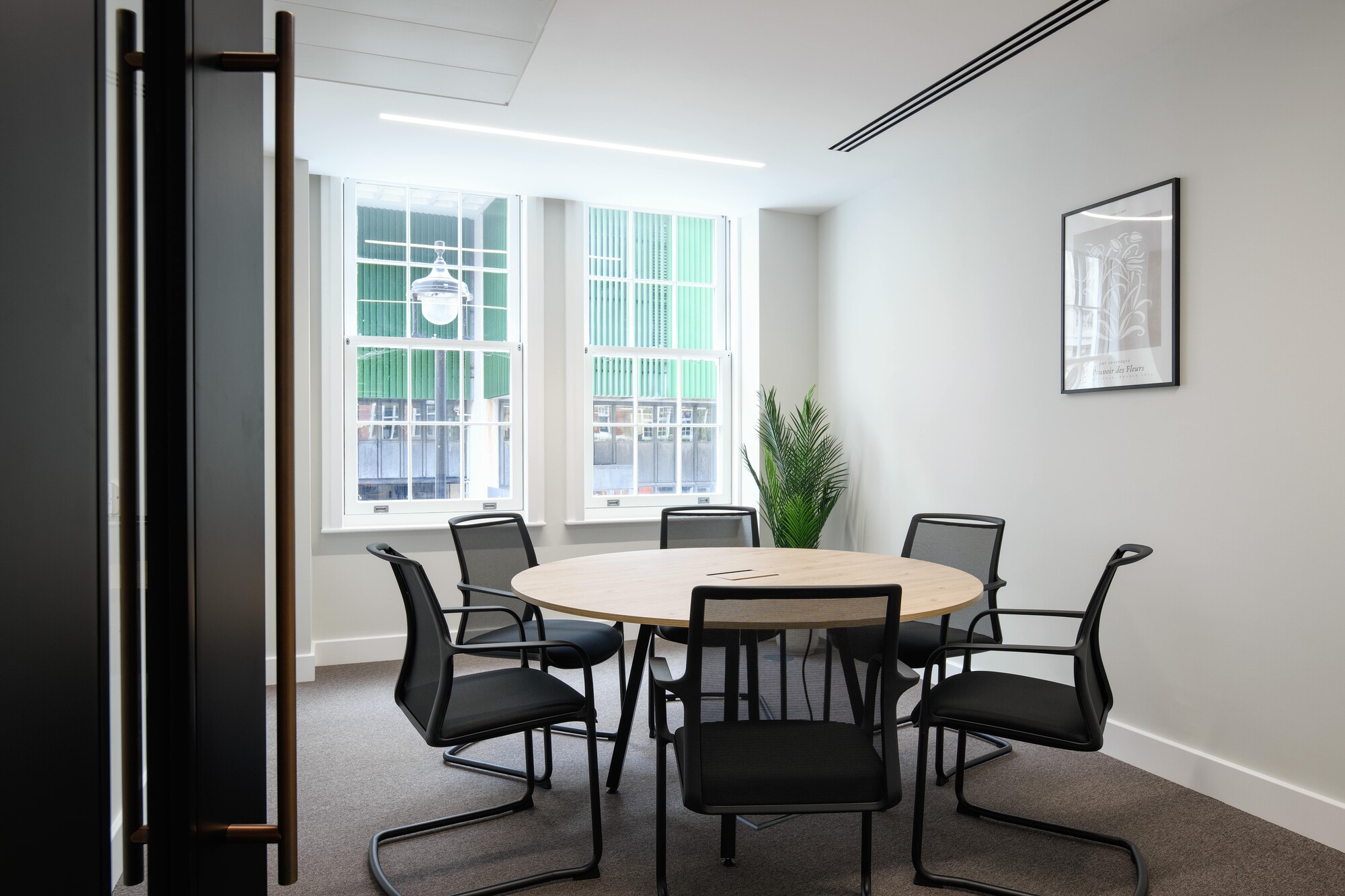 Round meeting room table and black mesh chairs installed for an Asset Management Firm's Tenant-Ready™ office, styled with minimalist finishes and natural light.