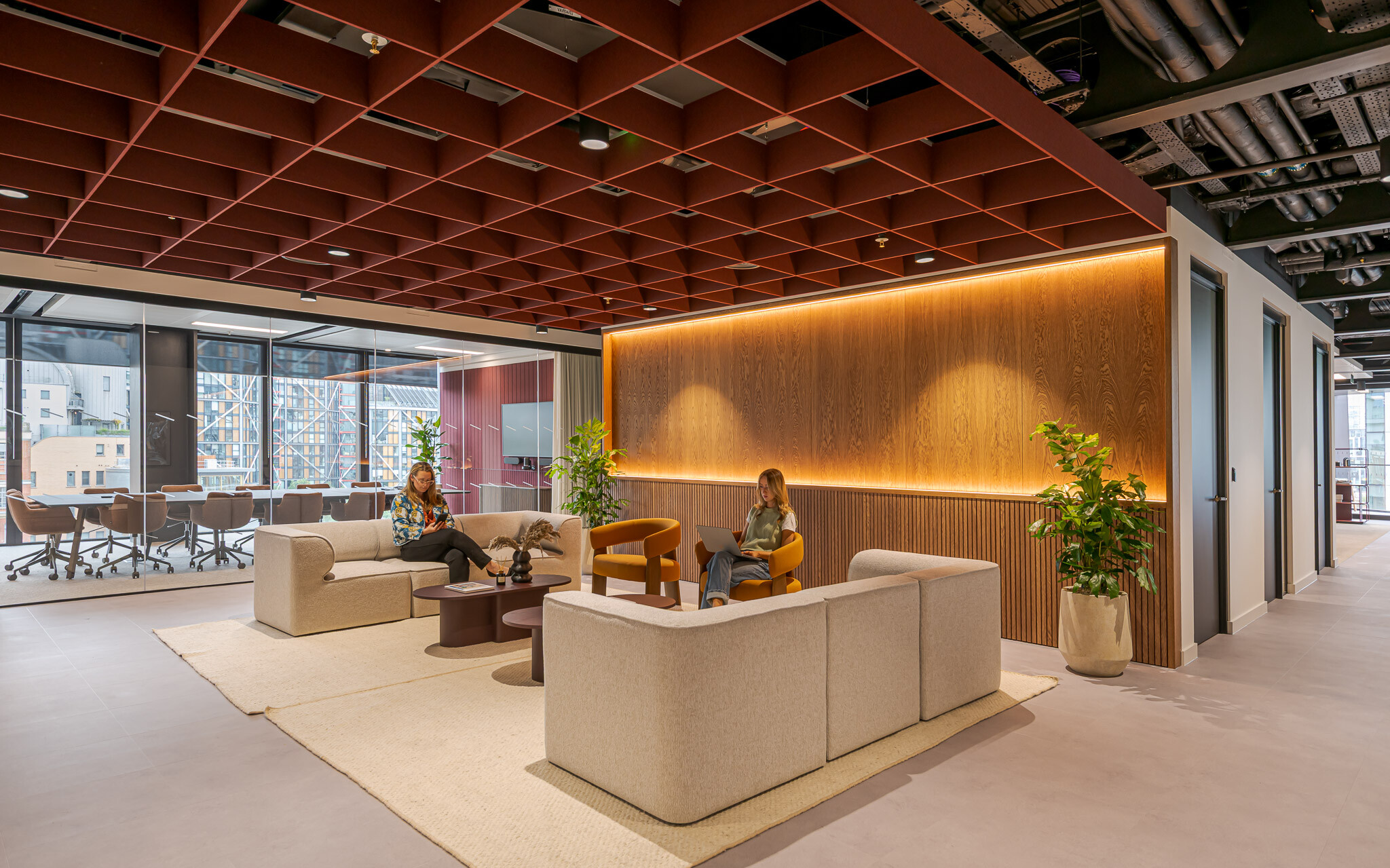 Tenant-Ready™ reception at Arbor furnished by Platfform, featuring soft neutral sofas, amber accent chairs, and round coffee tables beneath a red grid ceiling.