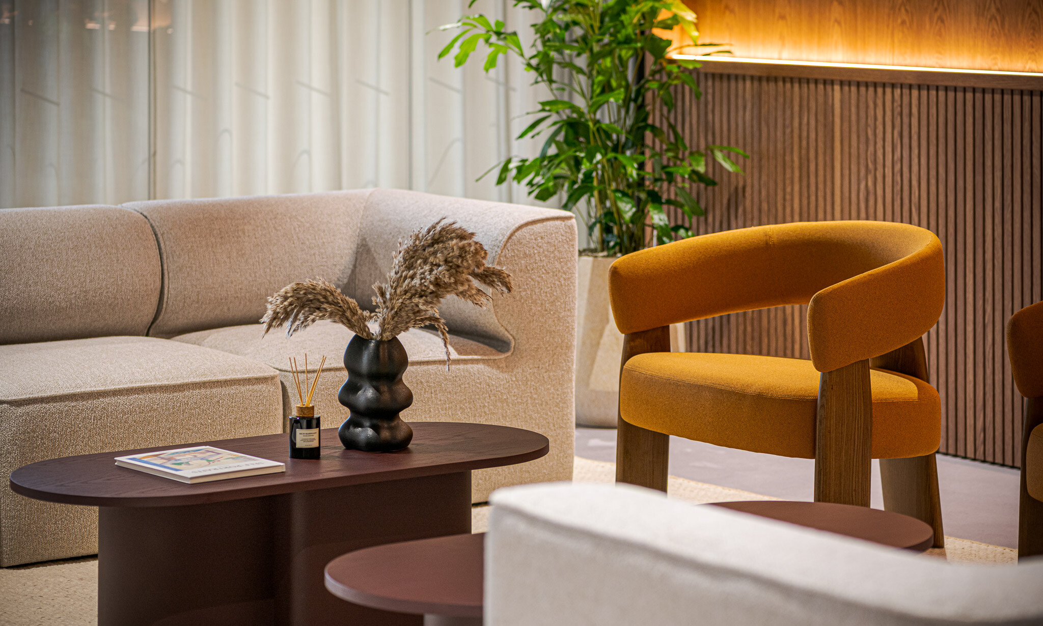 Close-up of Platfform’s furniture in the Arbor Tenant-Ready™ workspace, highlighting a warm-toned lounge chair, neutral sofa and styled coffee table with dried stems and incense.
